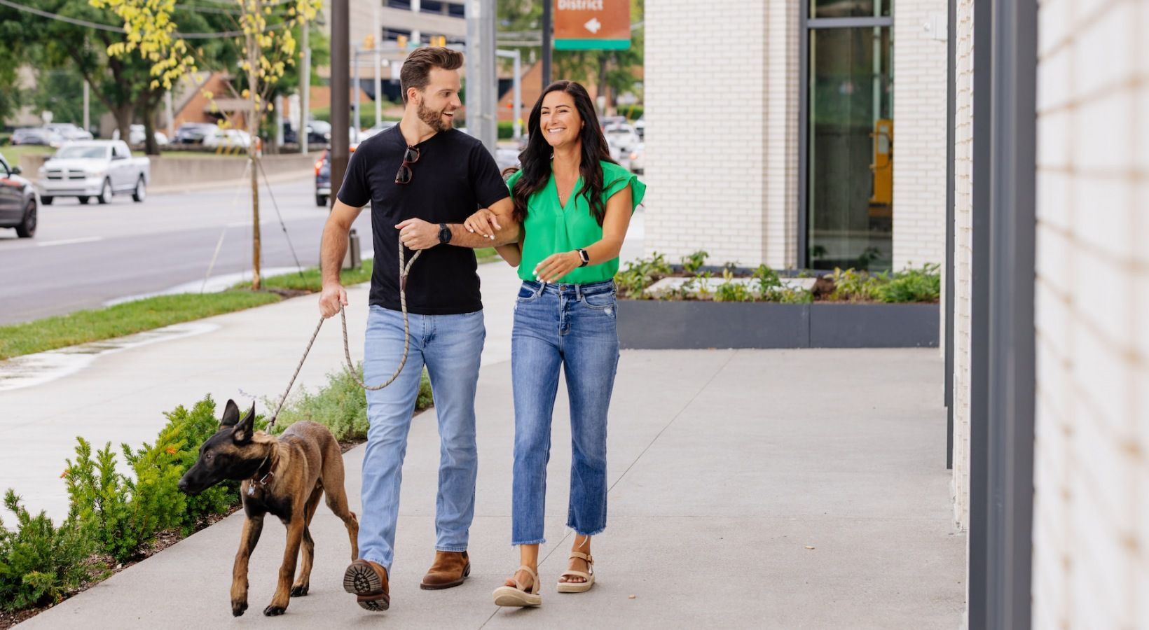 A man and a woman are walking a dog on a leash on a sidewalk.