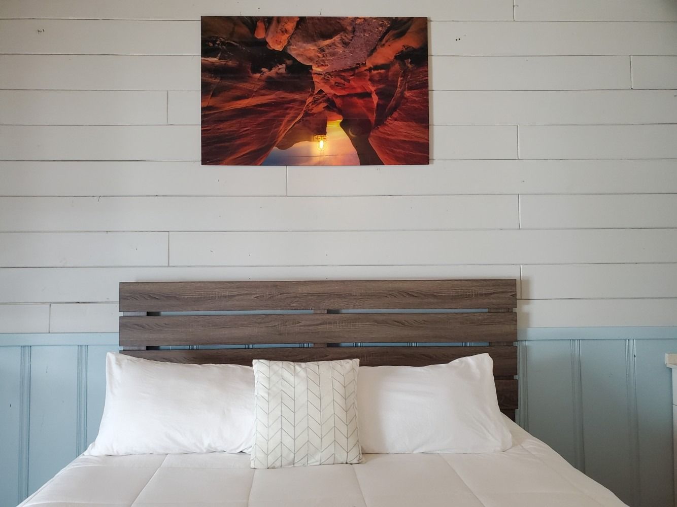 Bedroom with a bed, headboard, white linens, pillows, artwork, and light blue and white wall.