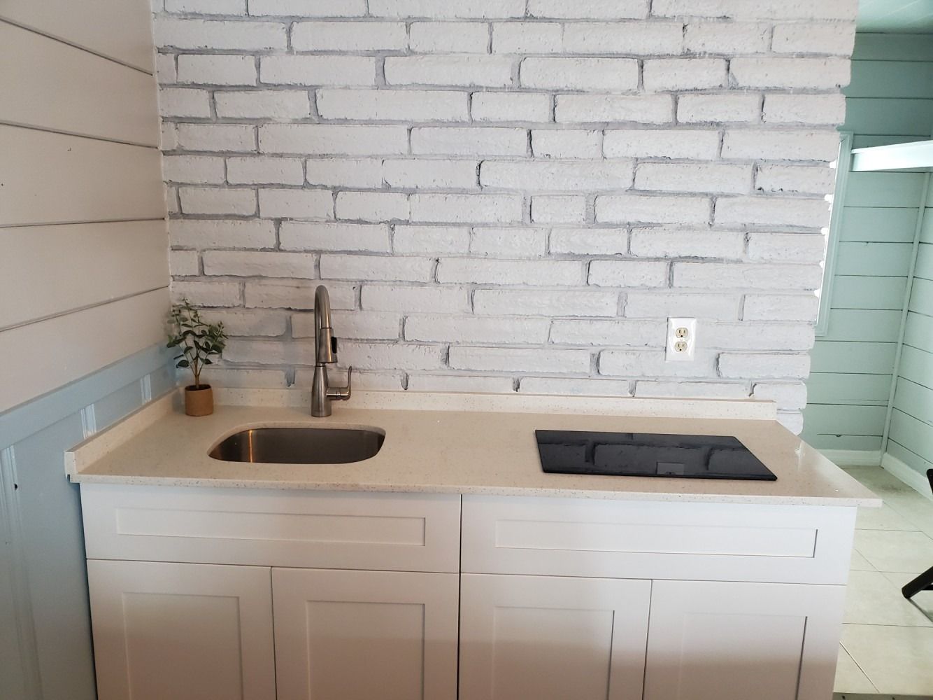 White kitchen with sink, cooktop, and cabinet. White brick wall background.