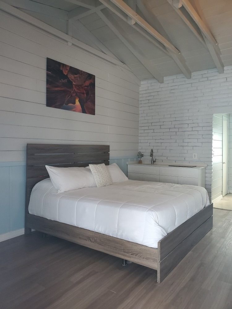 Bedroom with a bed, white walls, art, and a dresser.