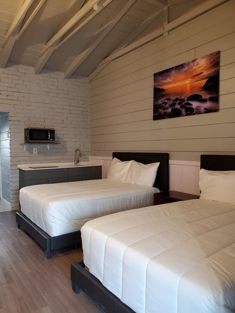 Two queen beds in a white-walled room with a microwave, sink, and sunset art.