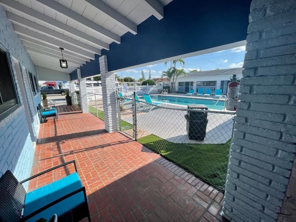 Covered walkway with brick floor, blue chairs, and view of a pool at a motel.