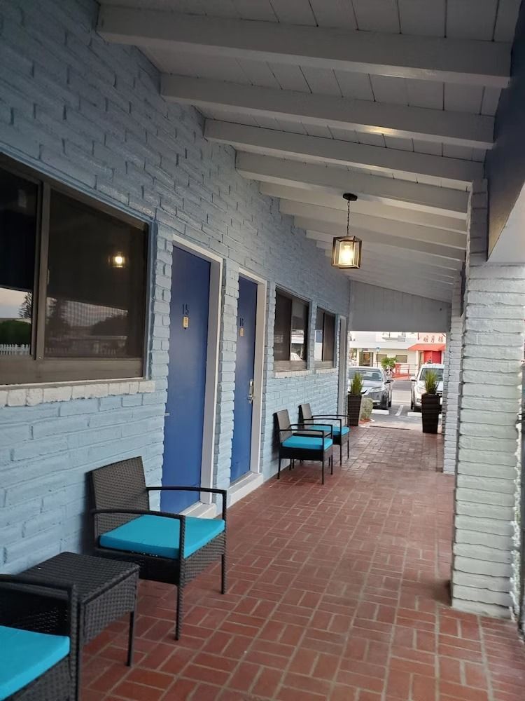 Exterior of a motel with blue brick walls, blue doors, and seating under a covered walkway.