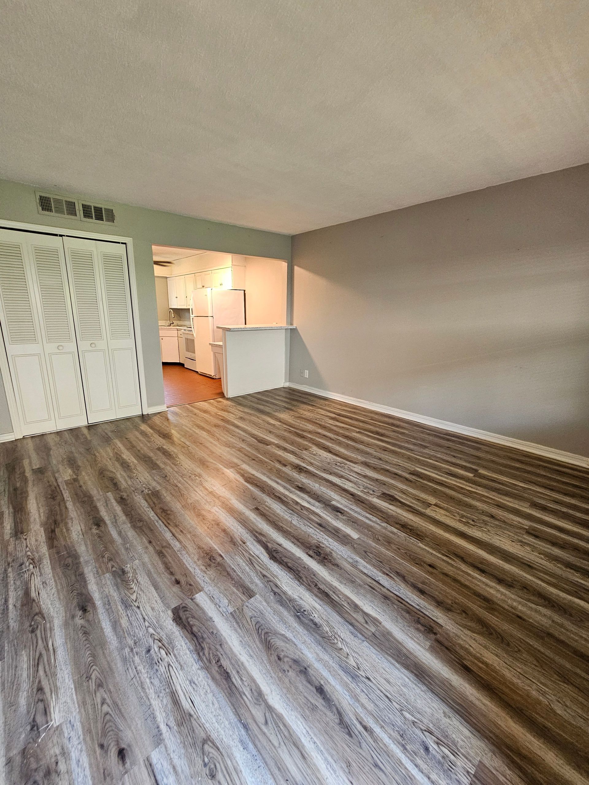 A living room with hardwood floors and a kitchen in the background.