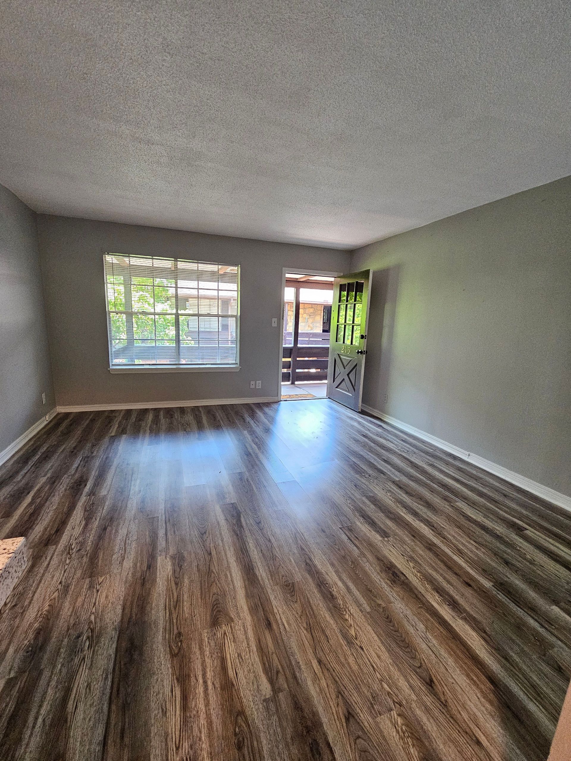 An empty living room with hardwood floors and a large window.