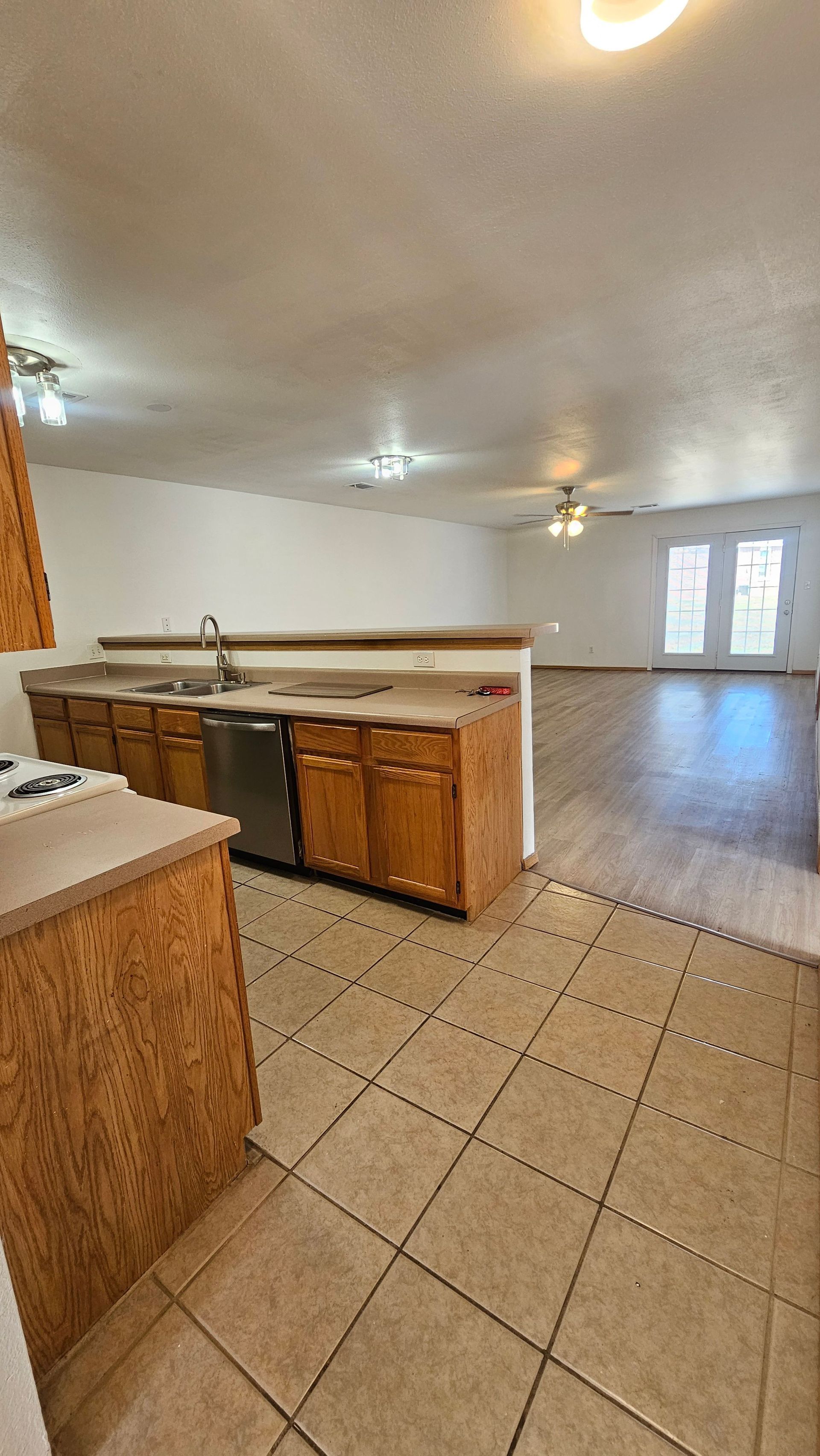 A kitchen with wooden cabinets , a dishwasher , a sink , and a tile floor.