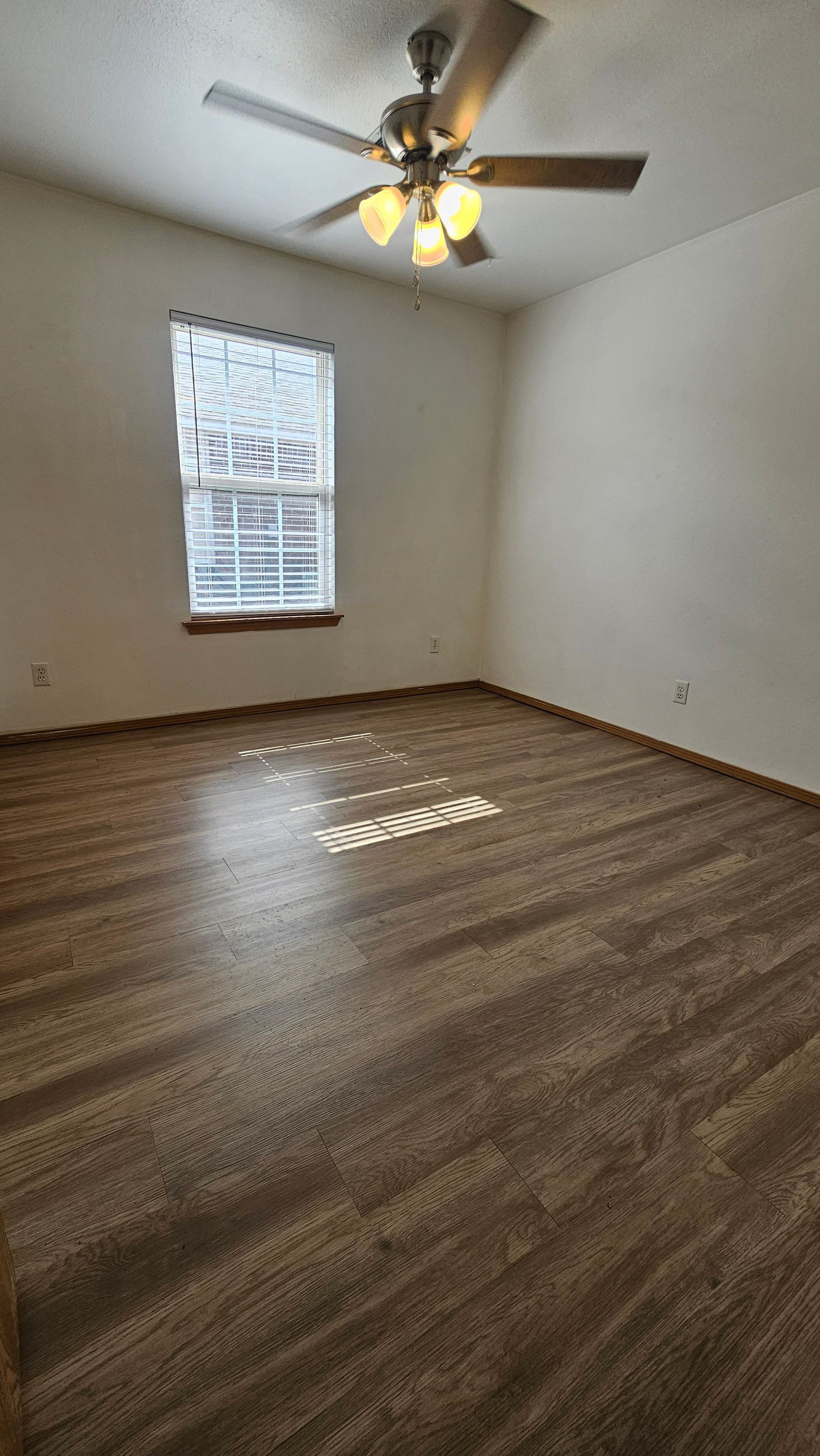 An empty room with a ceiling fan and a window.