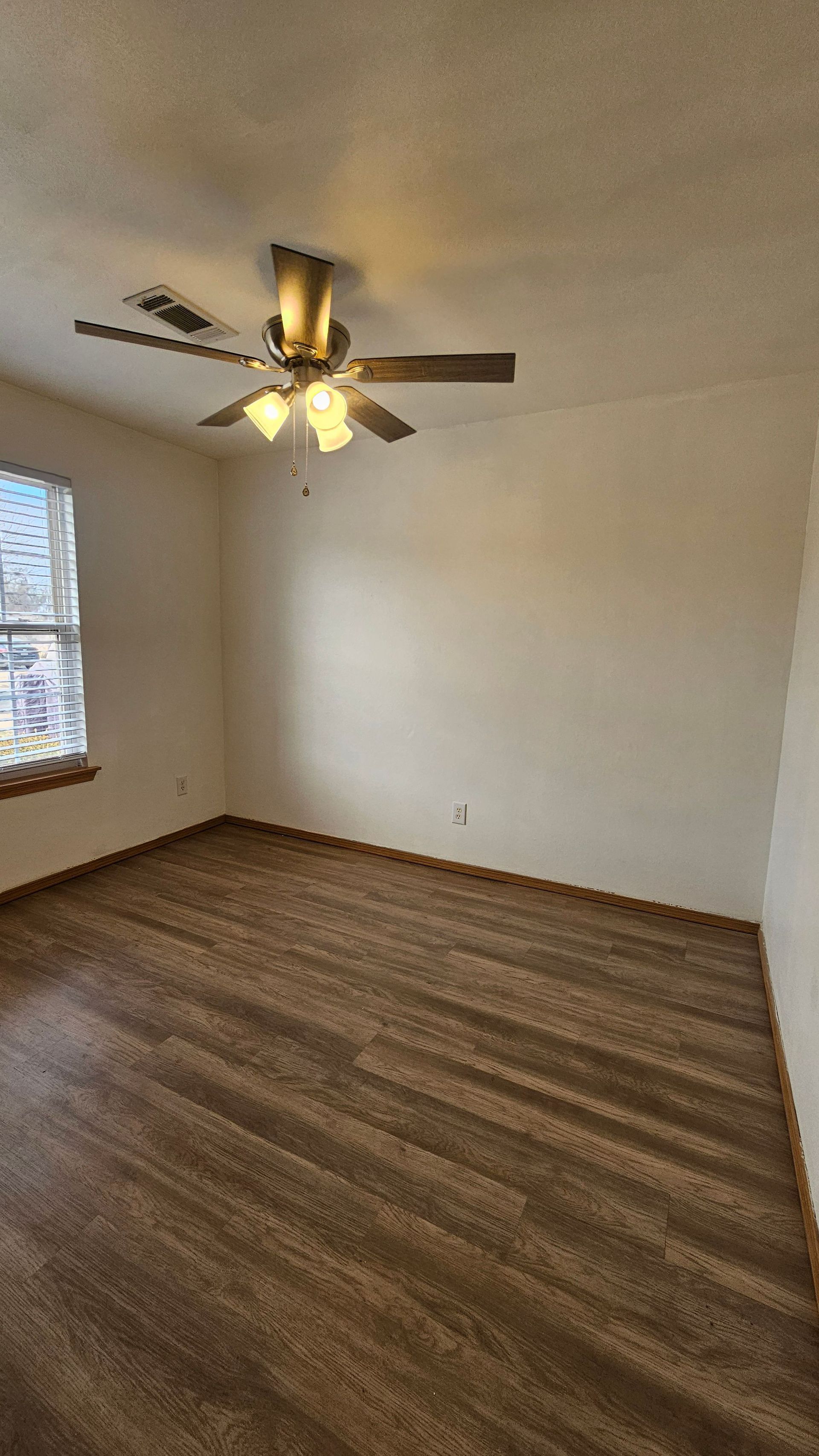 An empty room with a ceiling fan and a window.