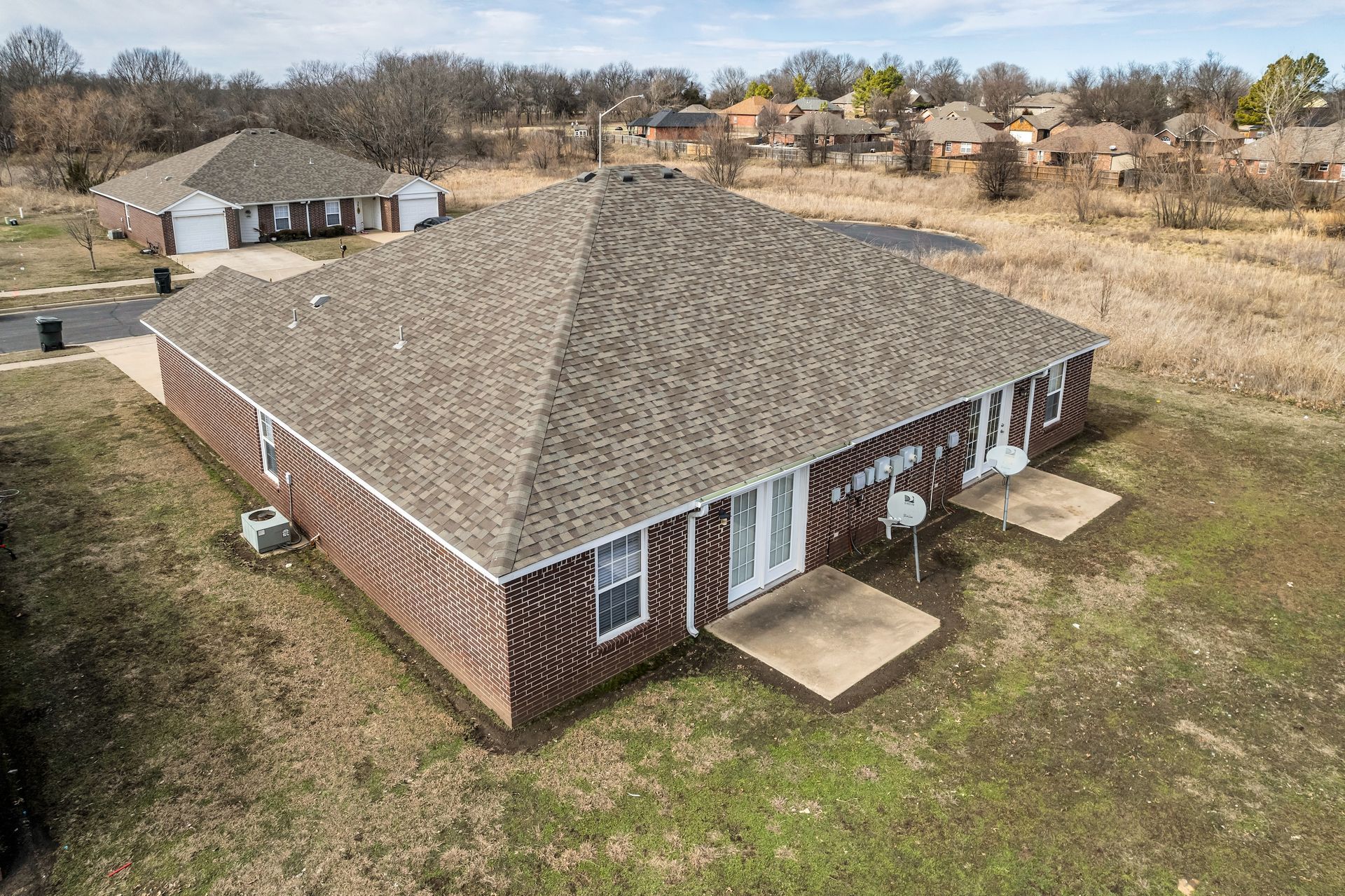 An aerial view of a brick house with a roof in a residential area.