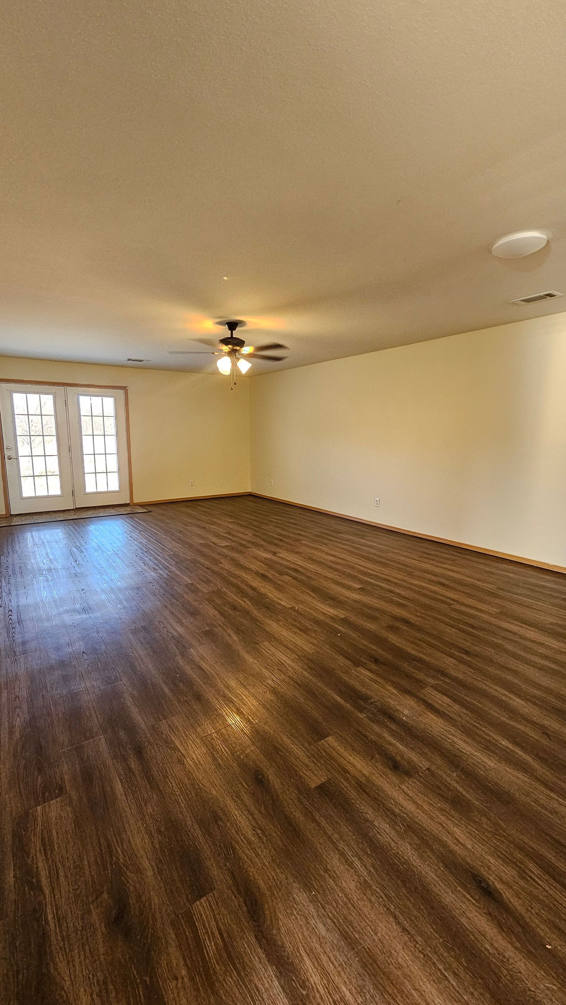An empty living room with hardwood floors and a ceiling fan.