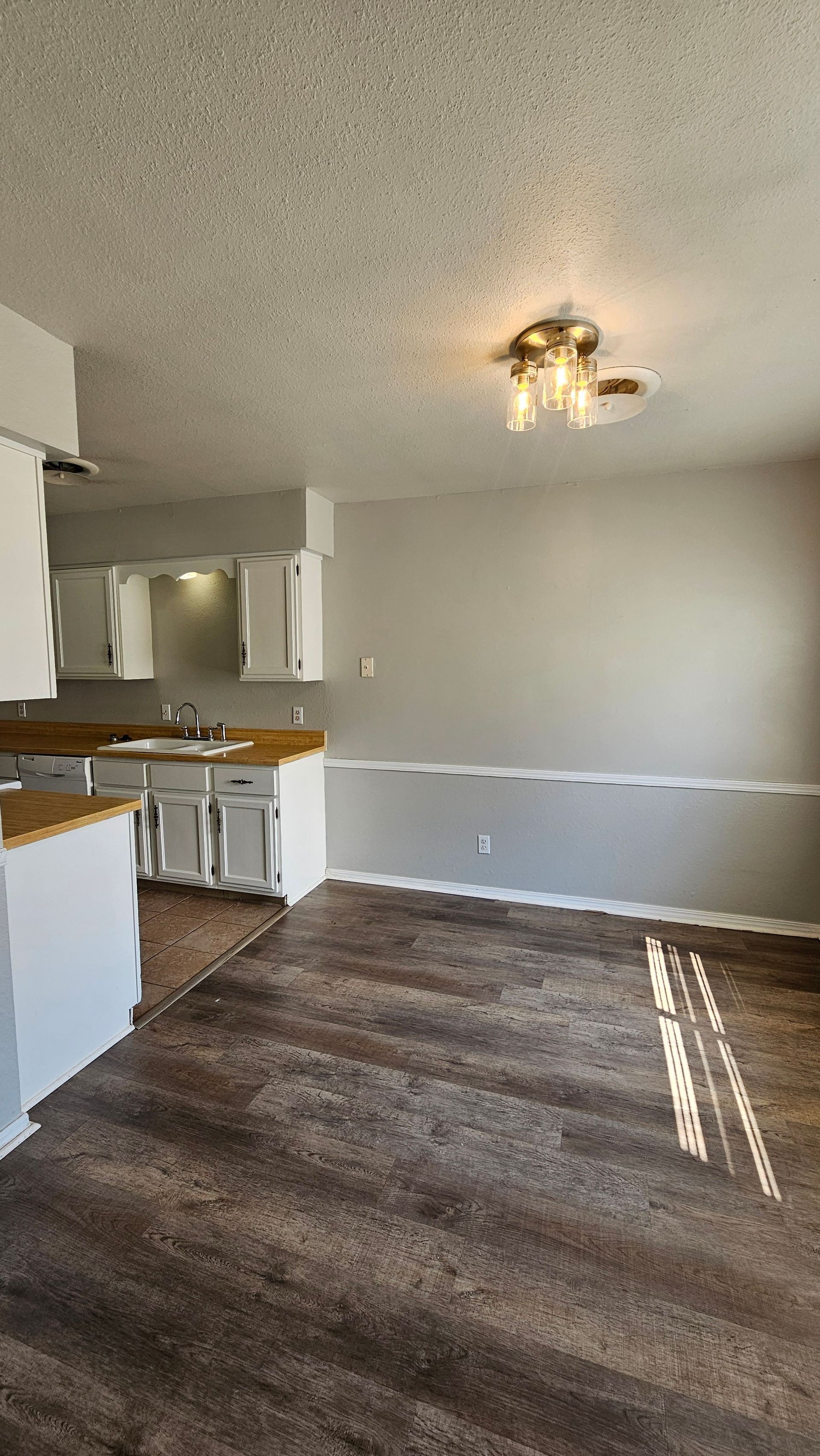 An empty living room with a kitchen in the background.