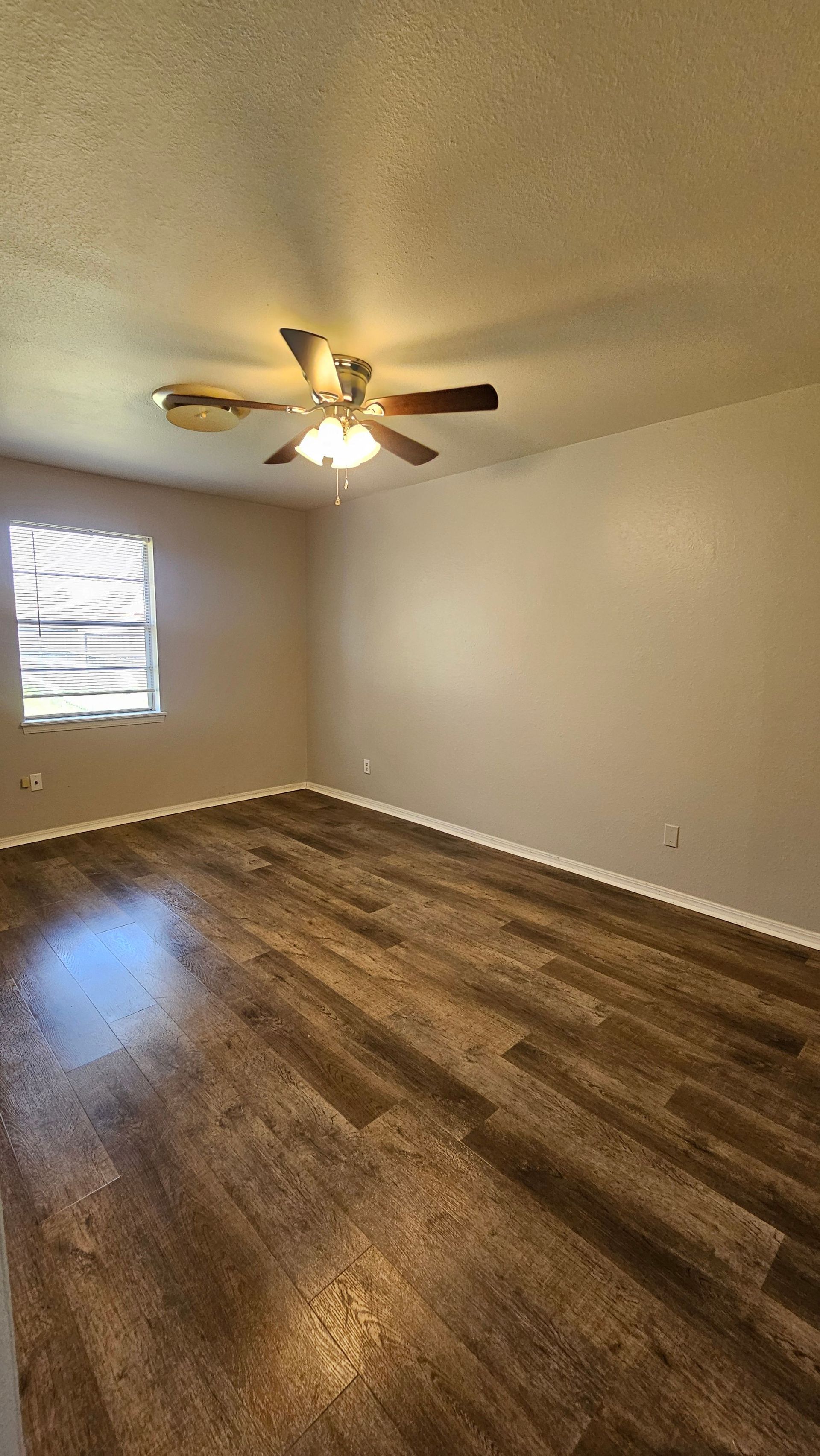 An empty living room with hardwood floors and a ceiling fan.