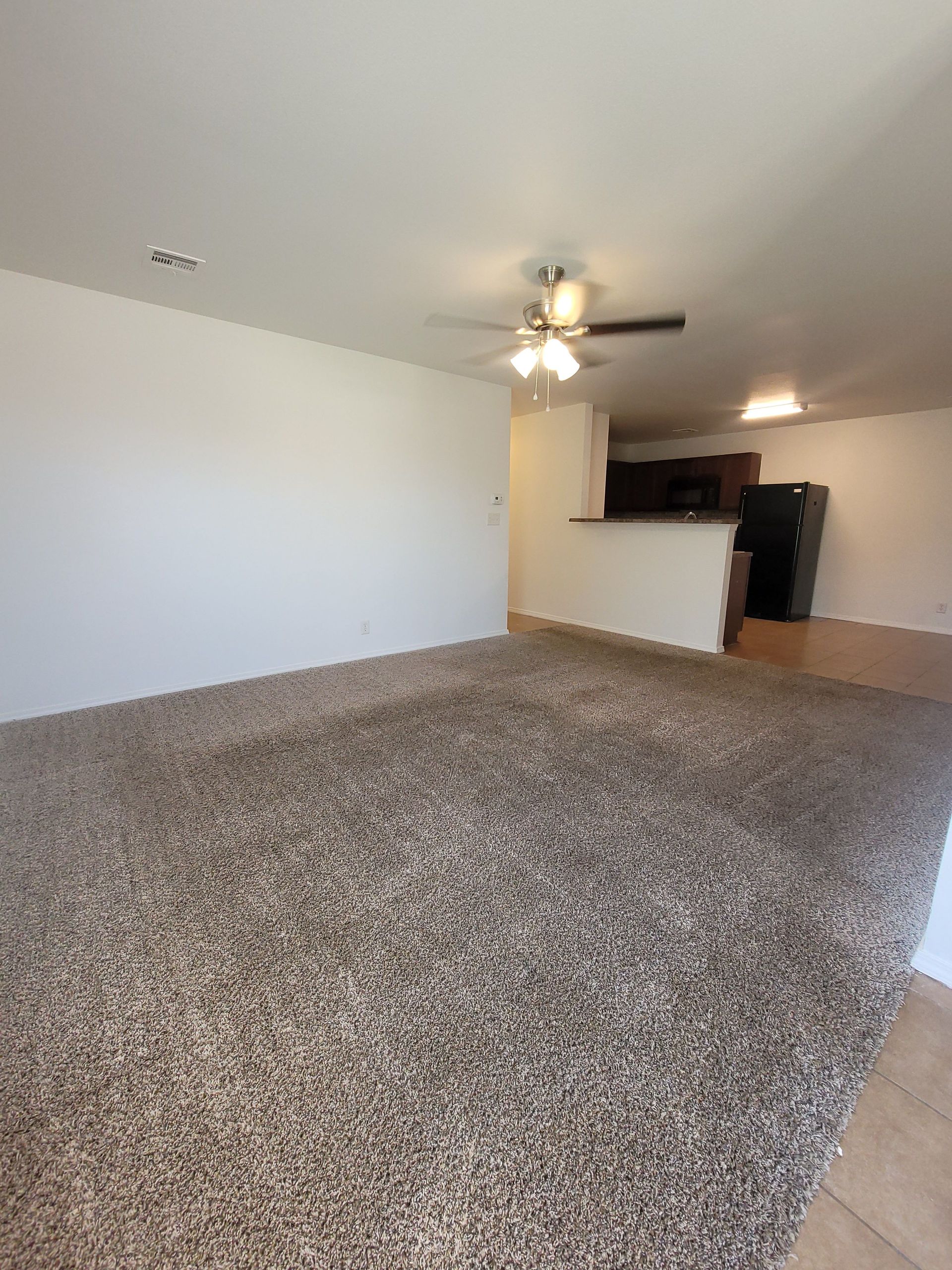 An empty living room with a ceiling fan and a carpeted floor.