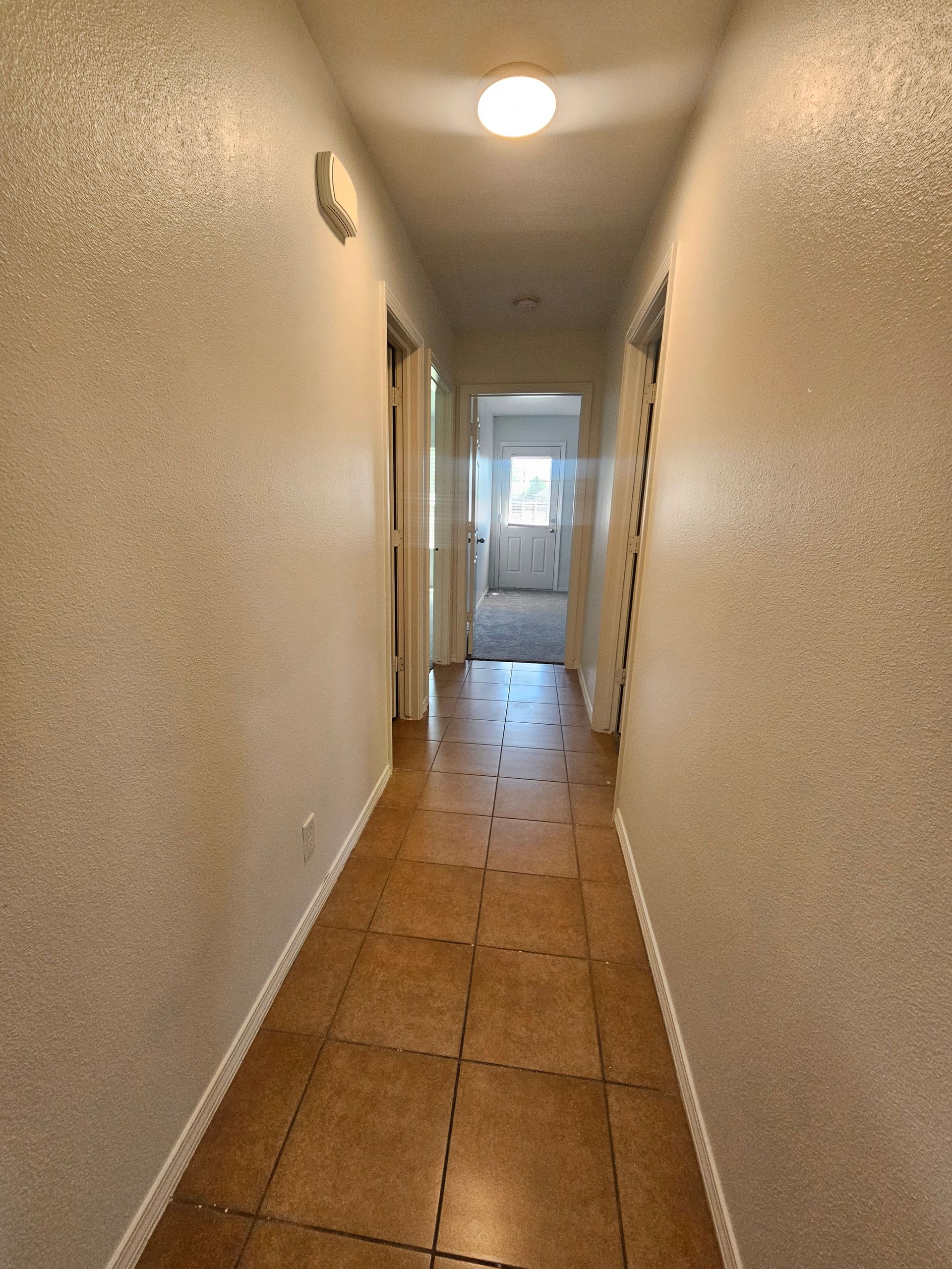 A long hallway with tile floors and white walls leading to a bedroom.