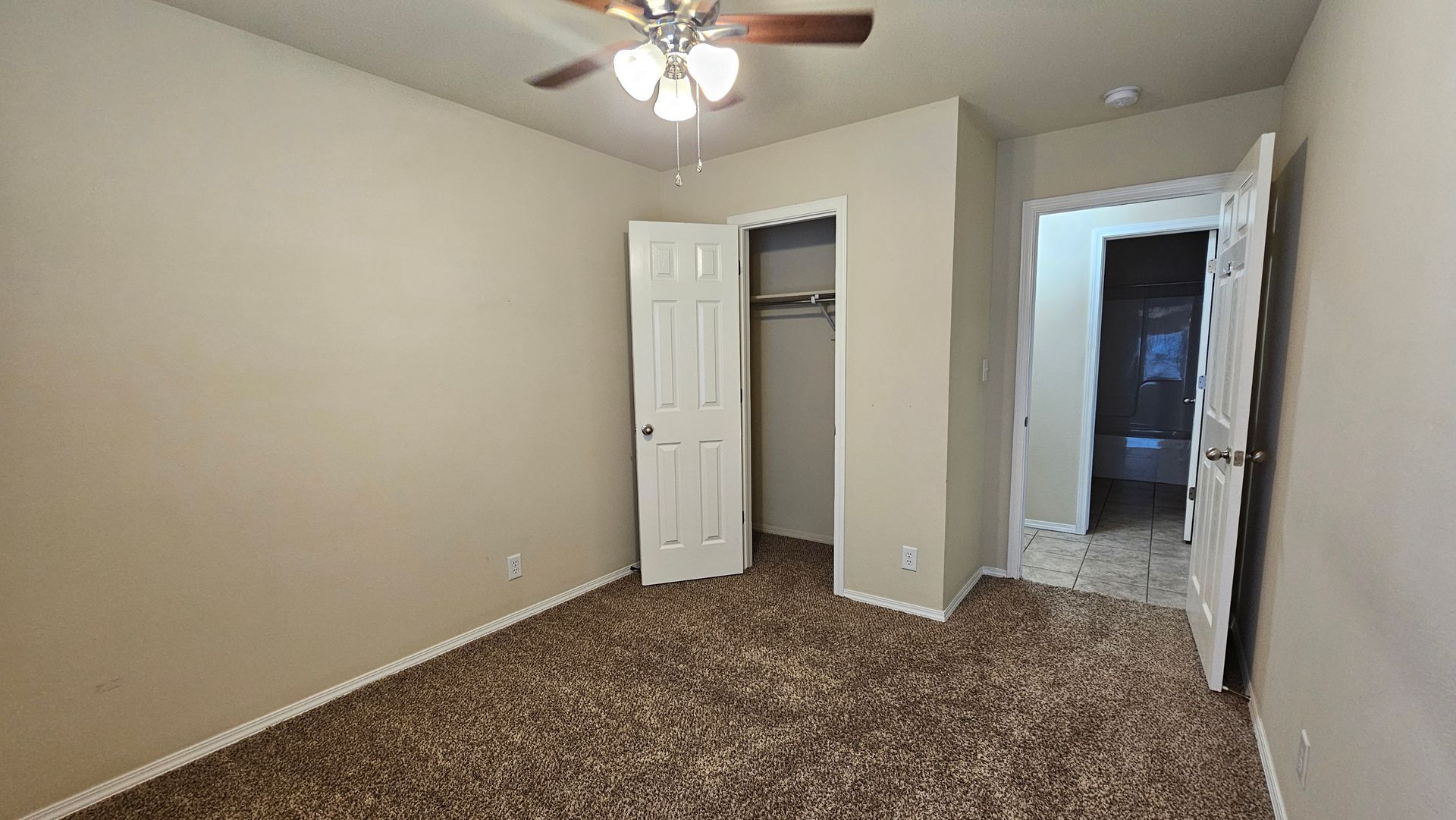 An empty bedroom with a ceiling fan and a closet.