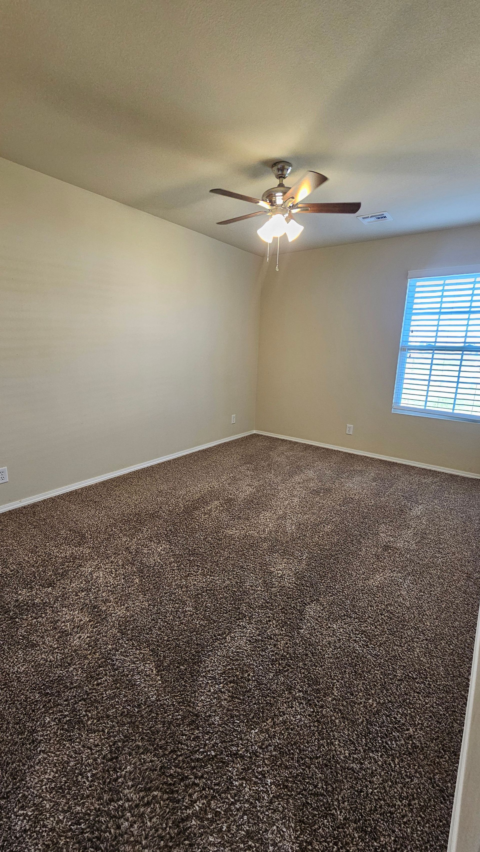 An empty bedroom with a ceiling fan and a window.