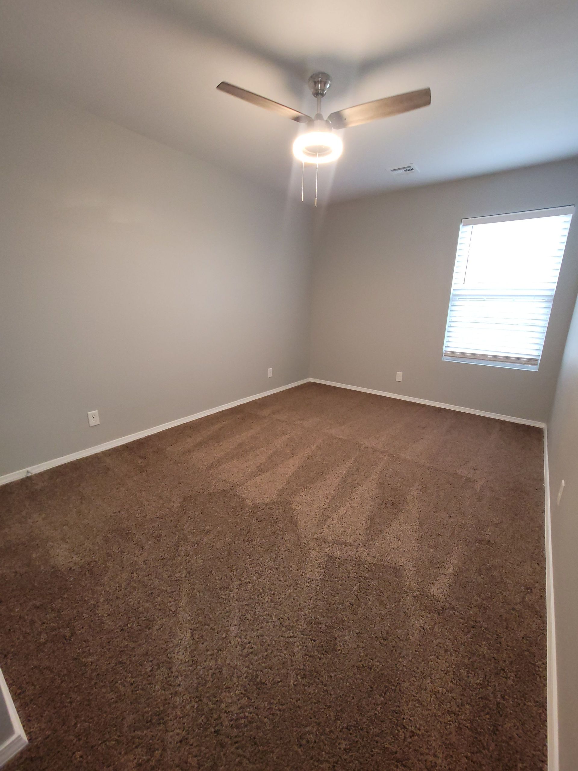 An empty bedroom with a ceiling fan and a window.