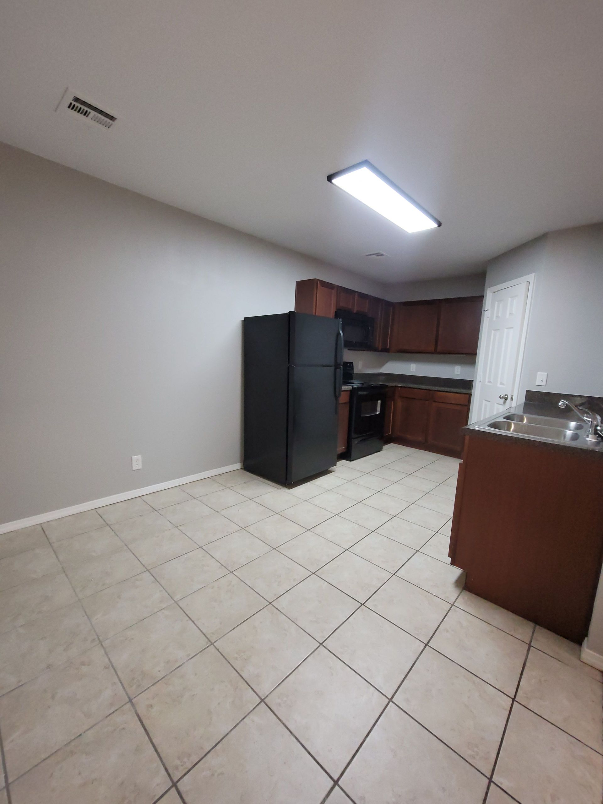 A kitchen with a black refrigerator , stove , sink and cabinets.