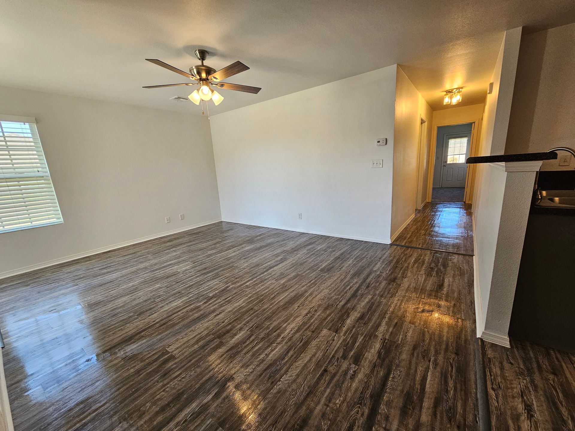 An empty living room with hardwood floors and a ceiling fan.