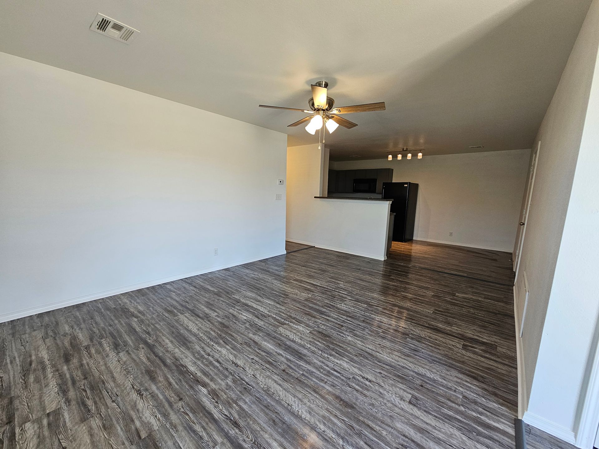 An empty living room with hardwood floors and a ceiling fan.