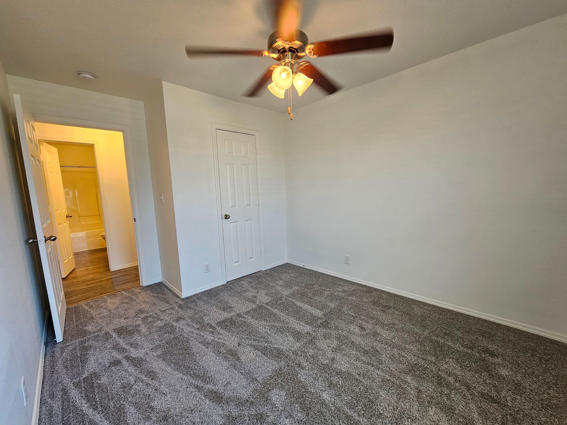 An empty bedroom with a ceiling fan and a carpeted floor.