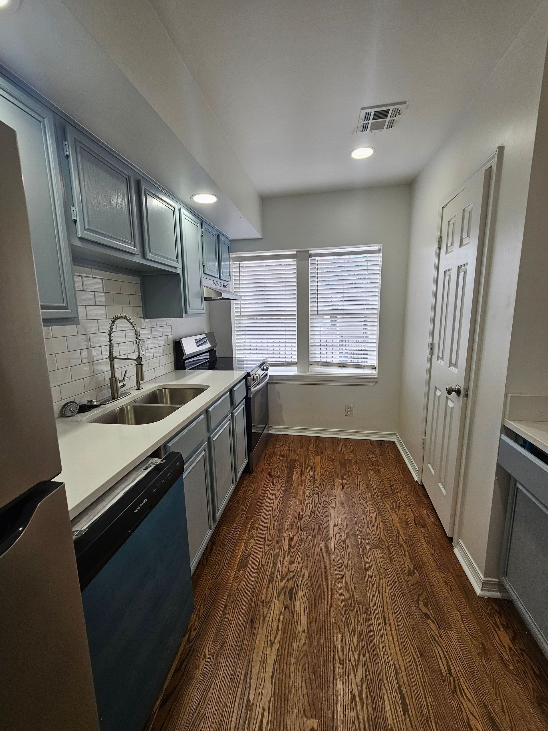 A kitchen with a sink , refrigerator , dishwasher , and two windows.