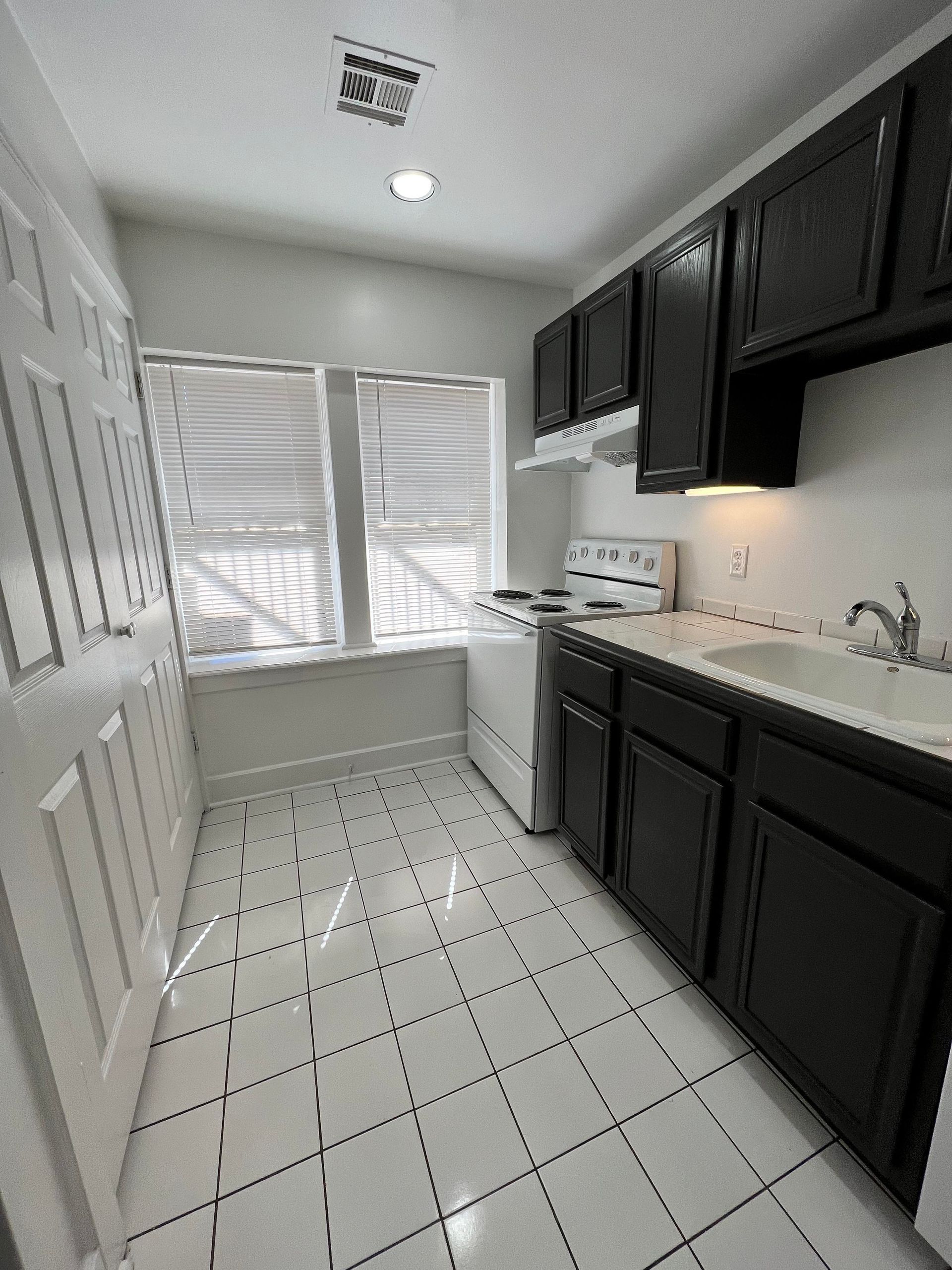 A kitchen with black cabinets , a stove , a sink , and a window.