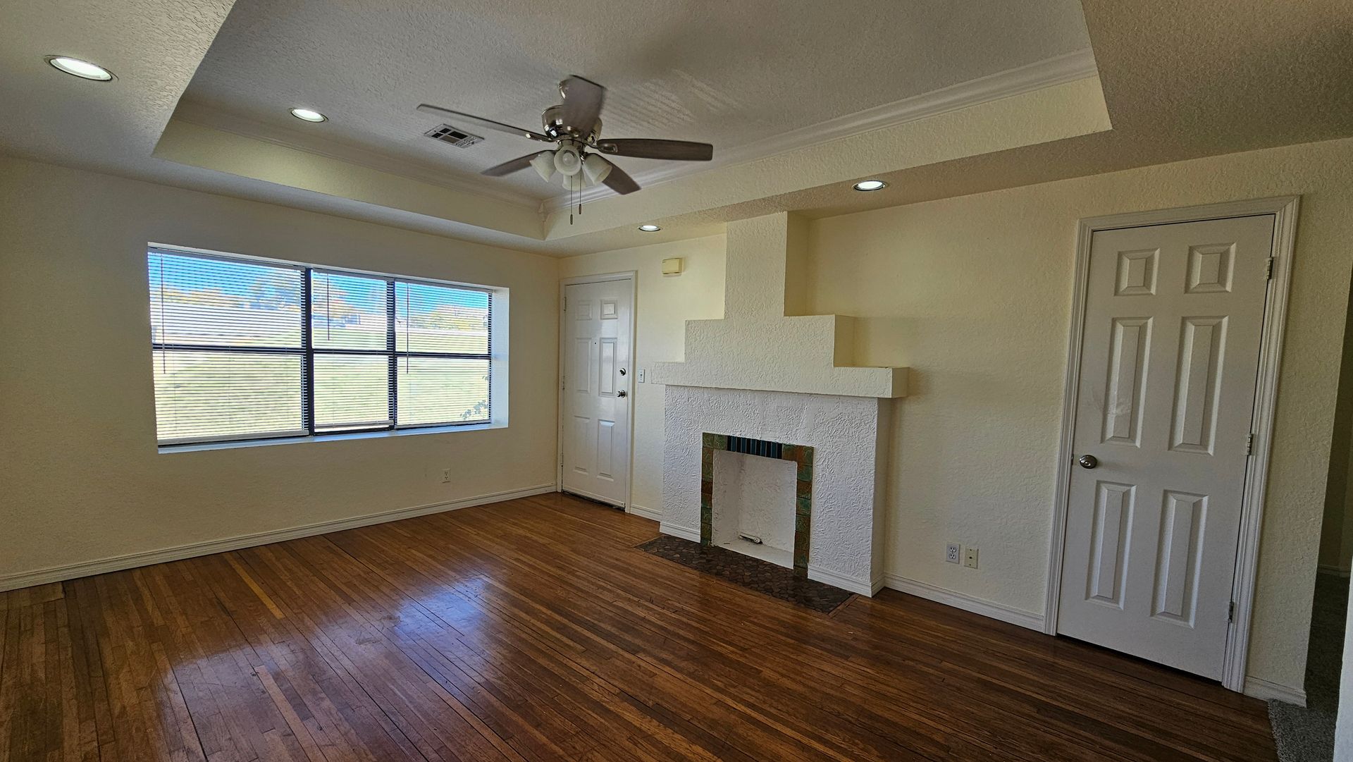 An empty living room with a fireplace and a ceiling fan.
