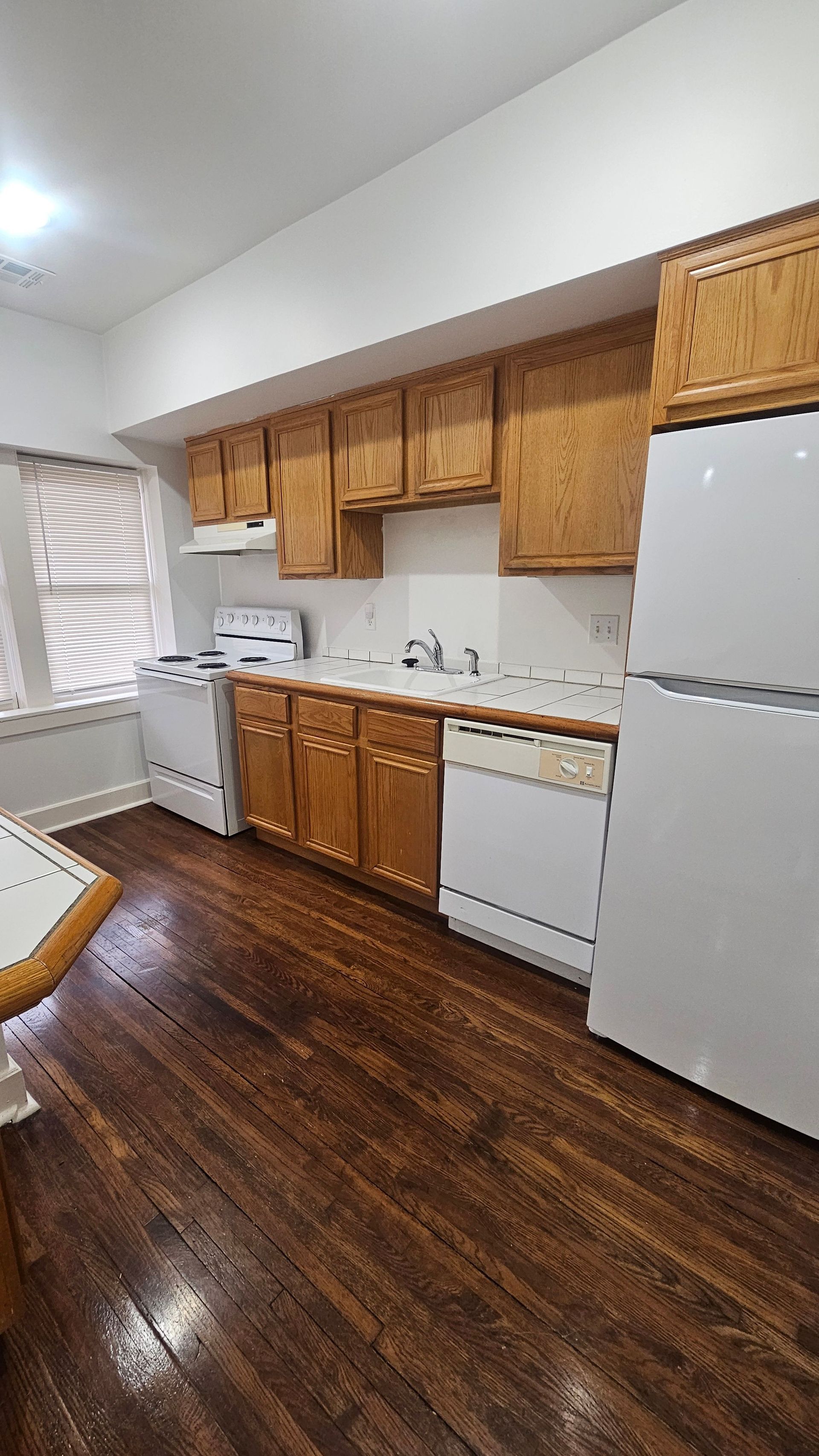 A kitchen with wooden cabinets , white appliances , and hardwood floors.