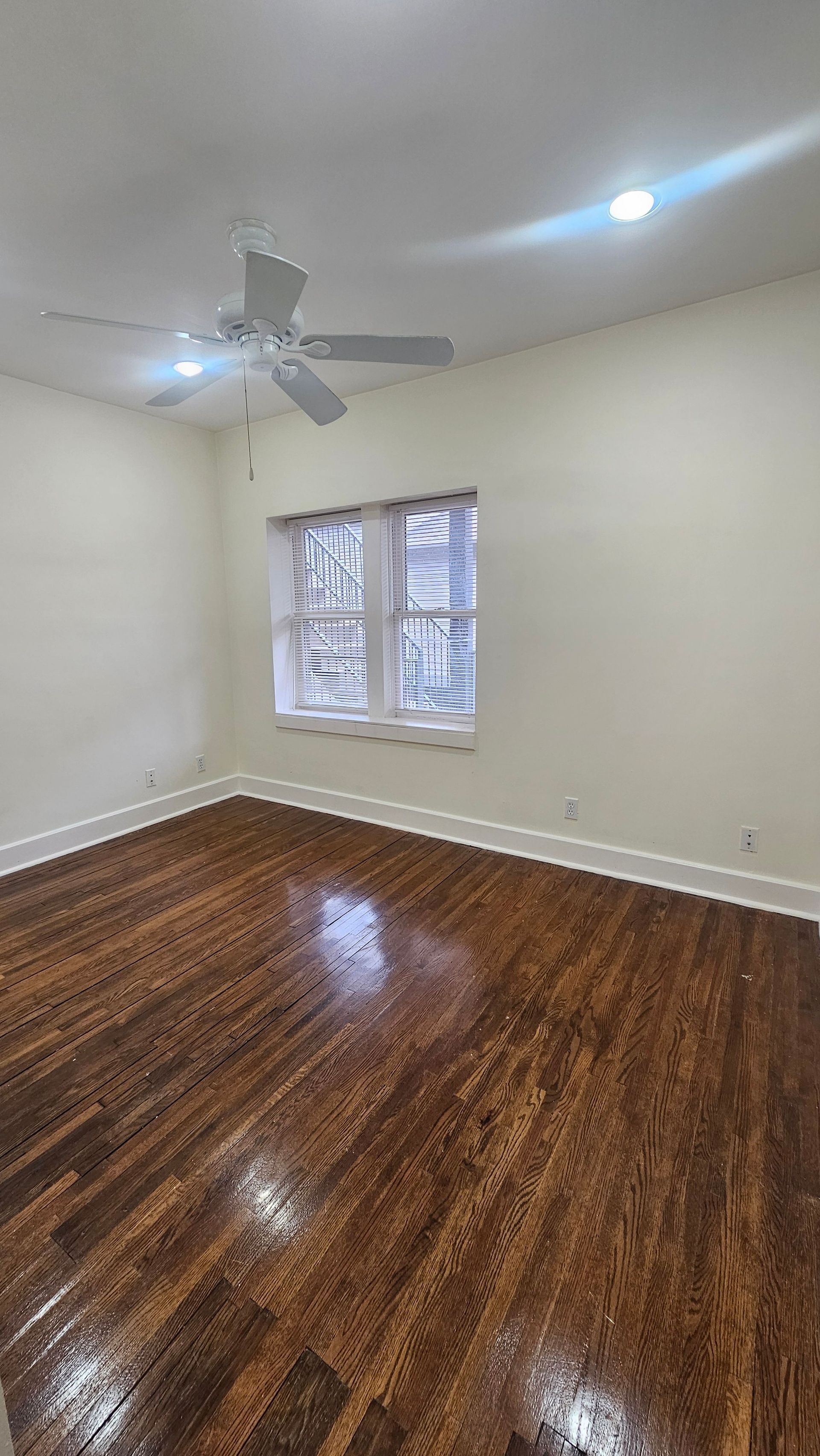 An empty room with hardwood floors and a ceiling fan.