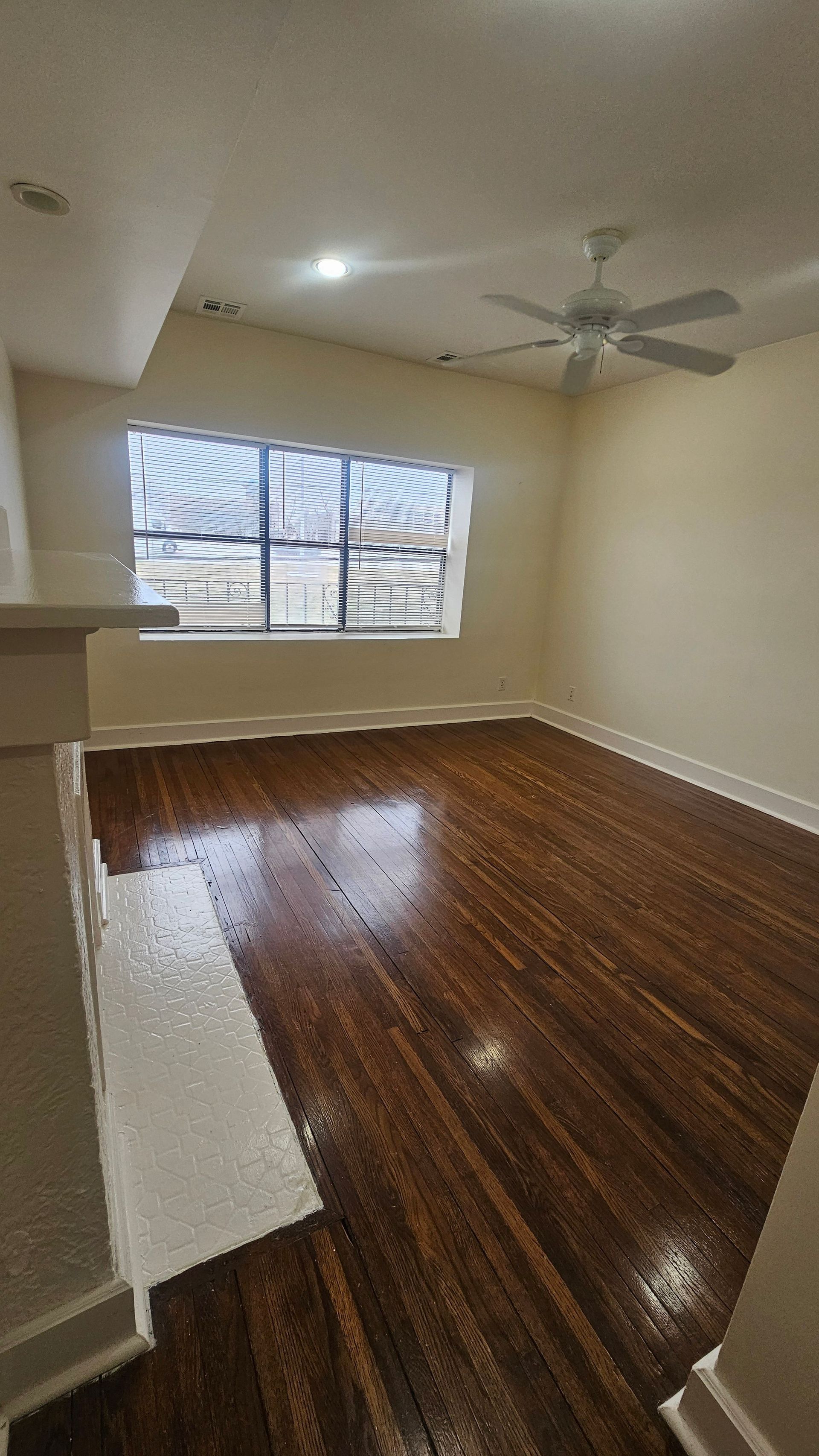 An empty living room with hardwood floors and a ceiling fan.