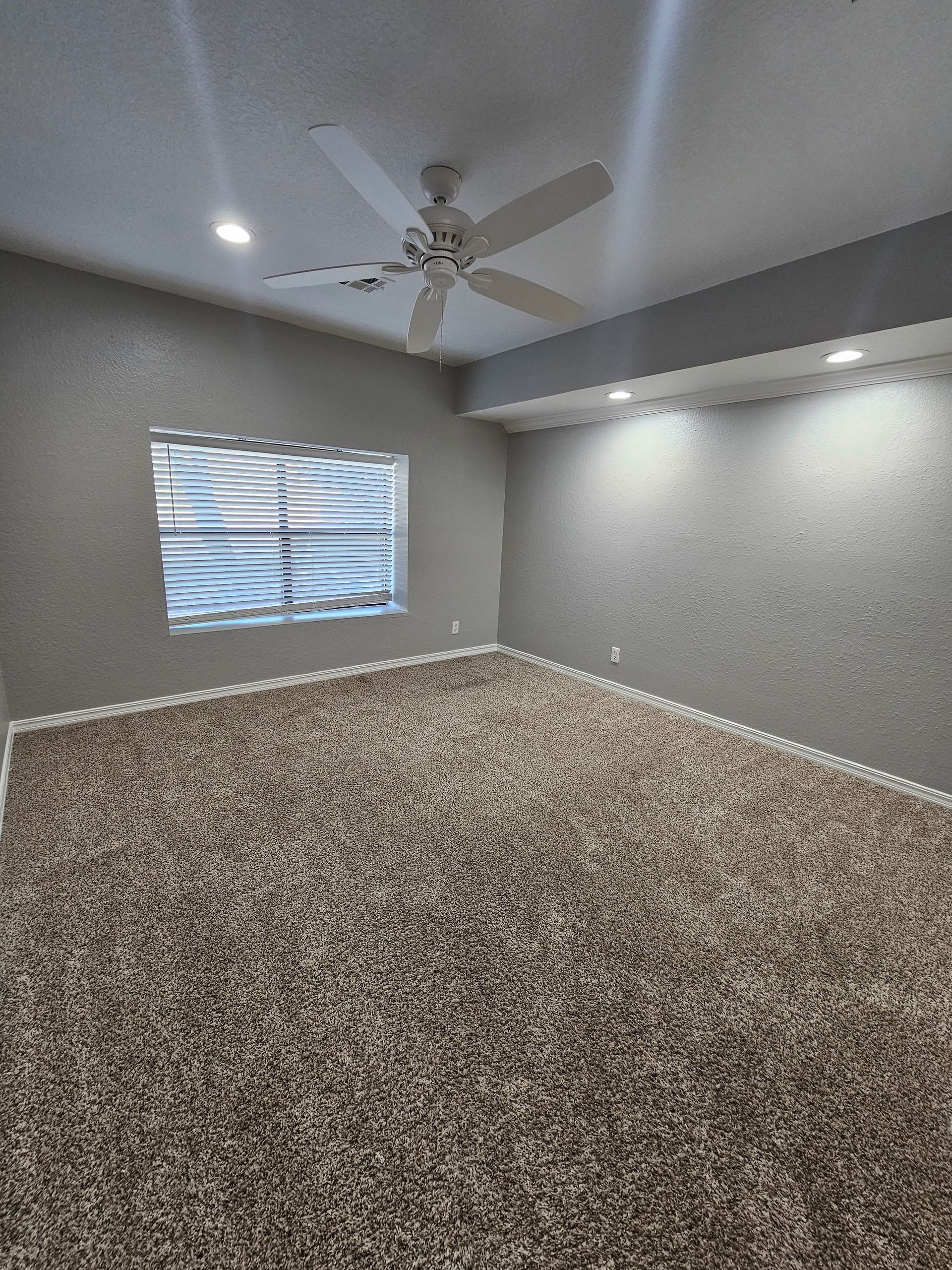 An empty bedroom with a ceiling fan and a window.