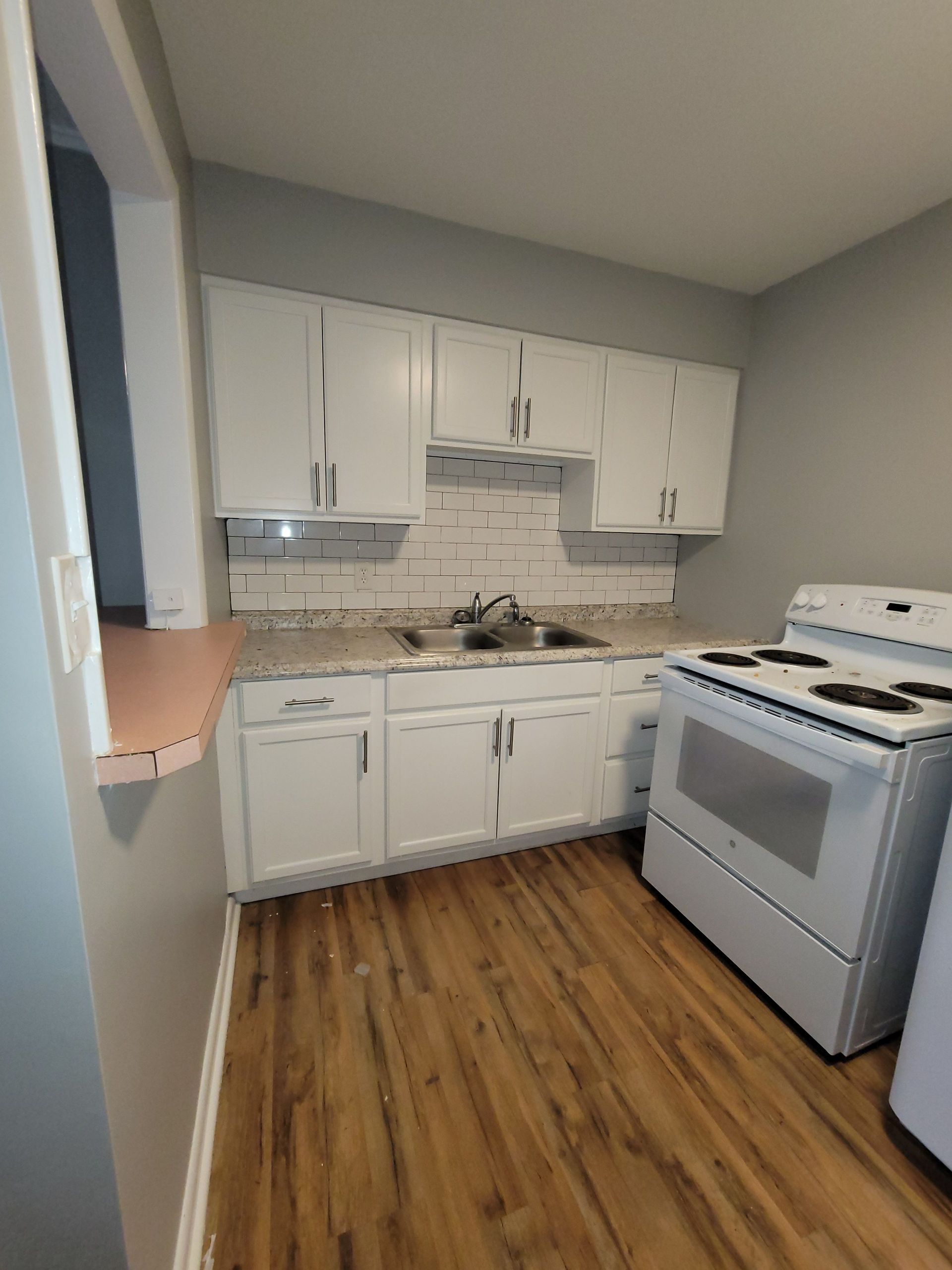 A kitchen with white cabinets , a white stove and a sink.