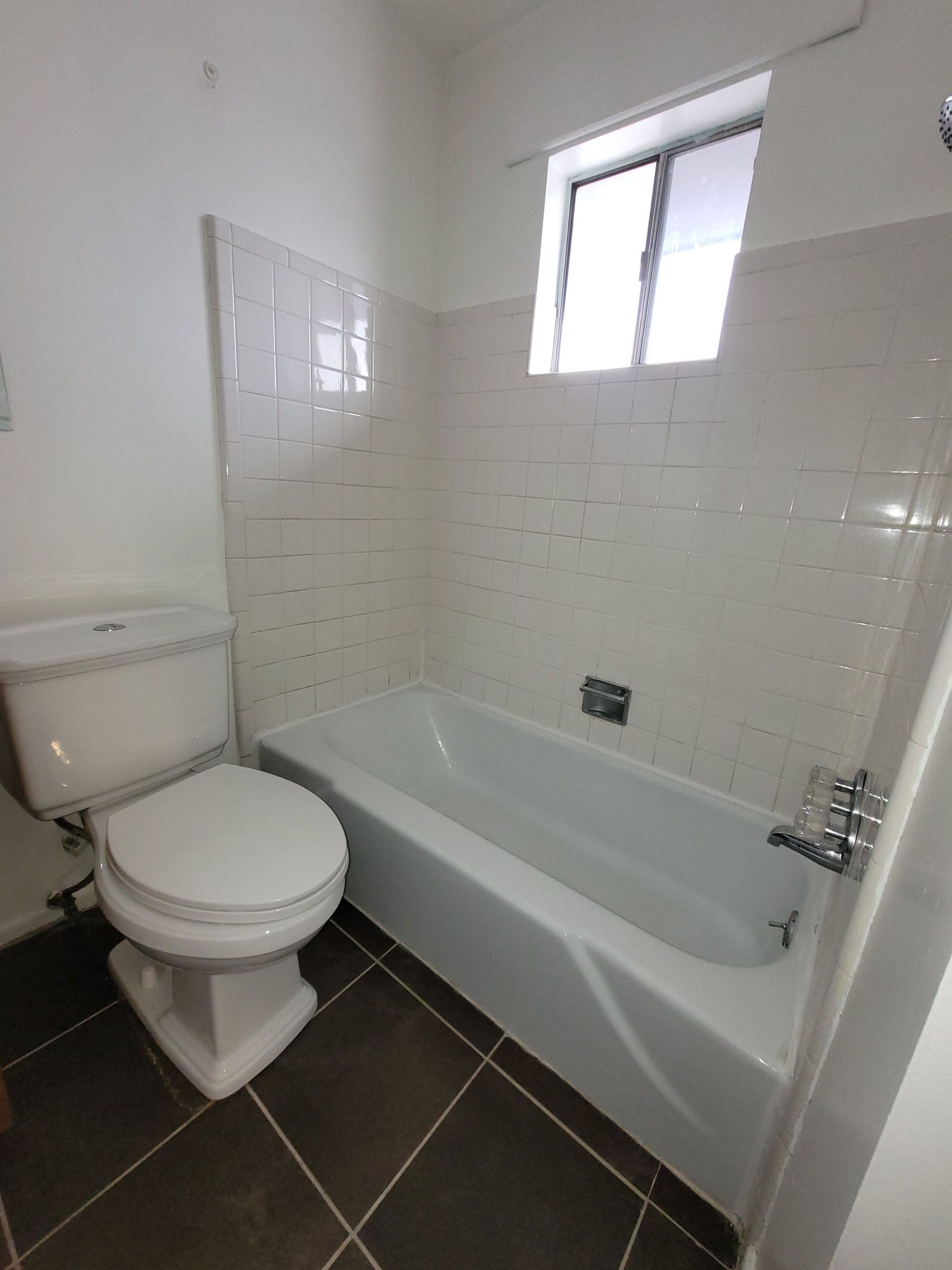 A bathroom with a toilet a tub and a window