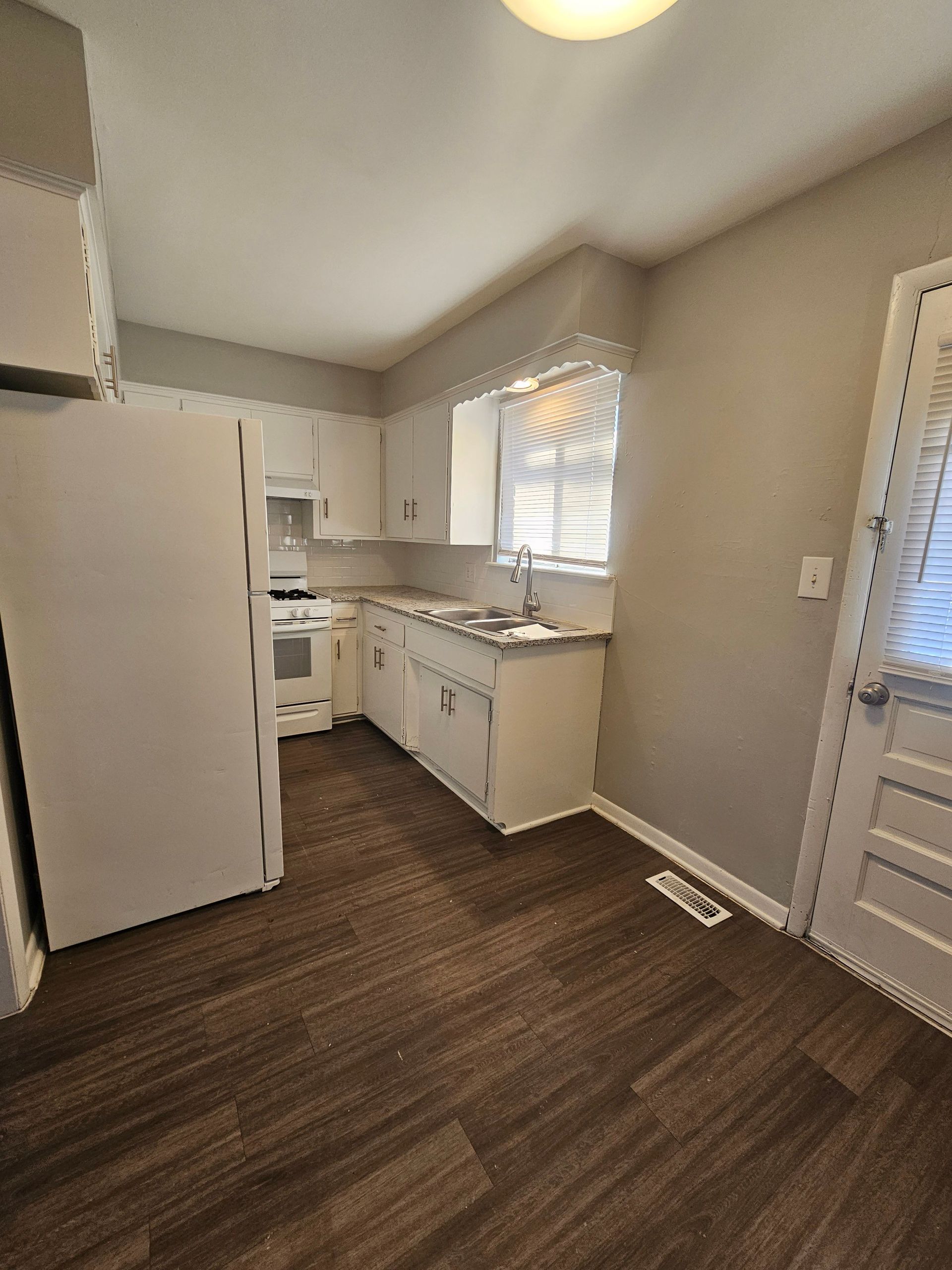 A kitchen with hardwood floors , white cabinets , a refrigerator , stove and sink.