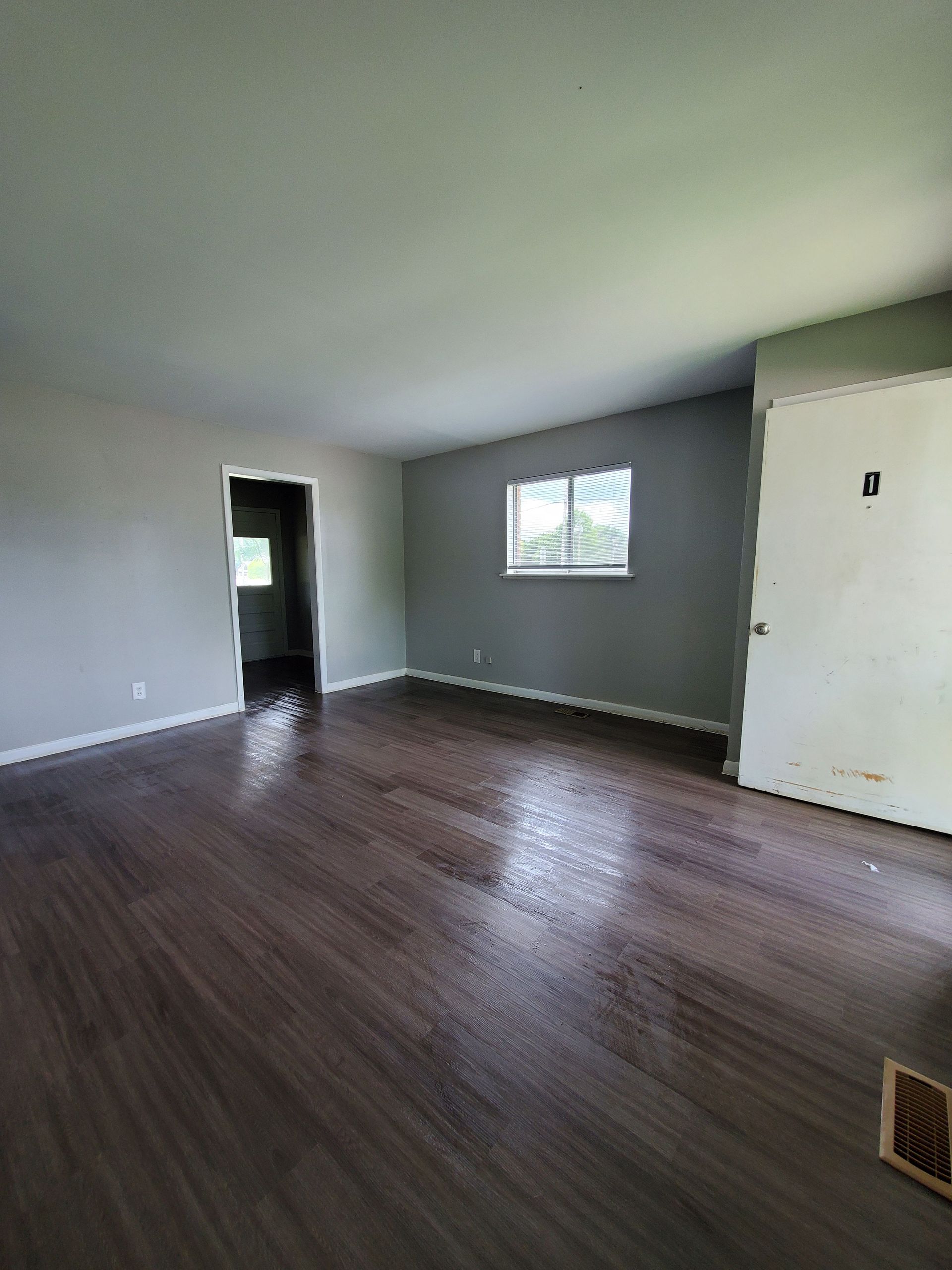 An empty living room with hardwood floors and a window.
