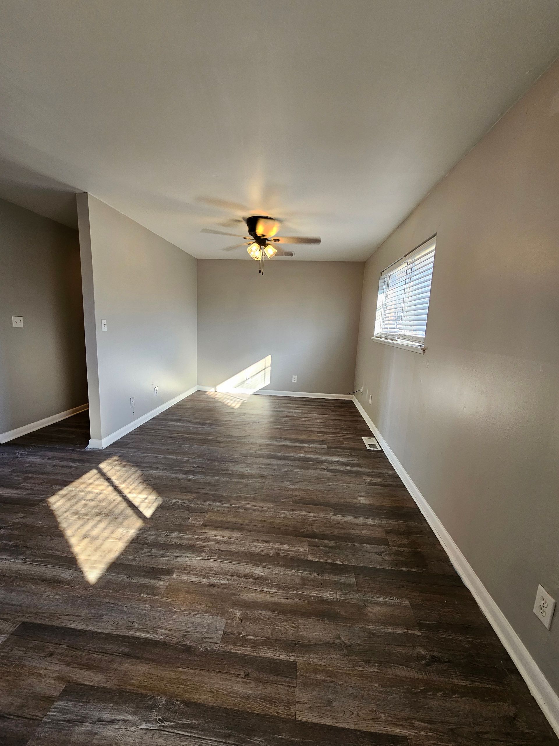 An empty living room with a ceiling fan and a window.