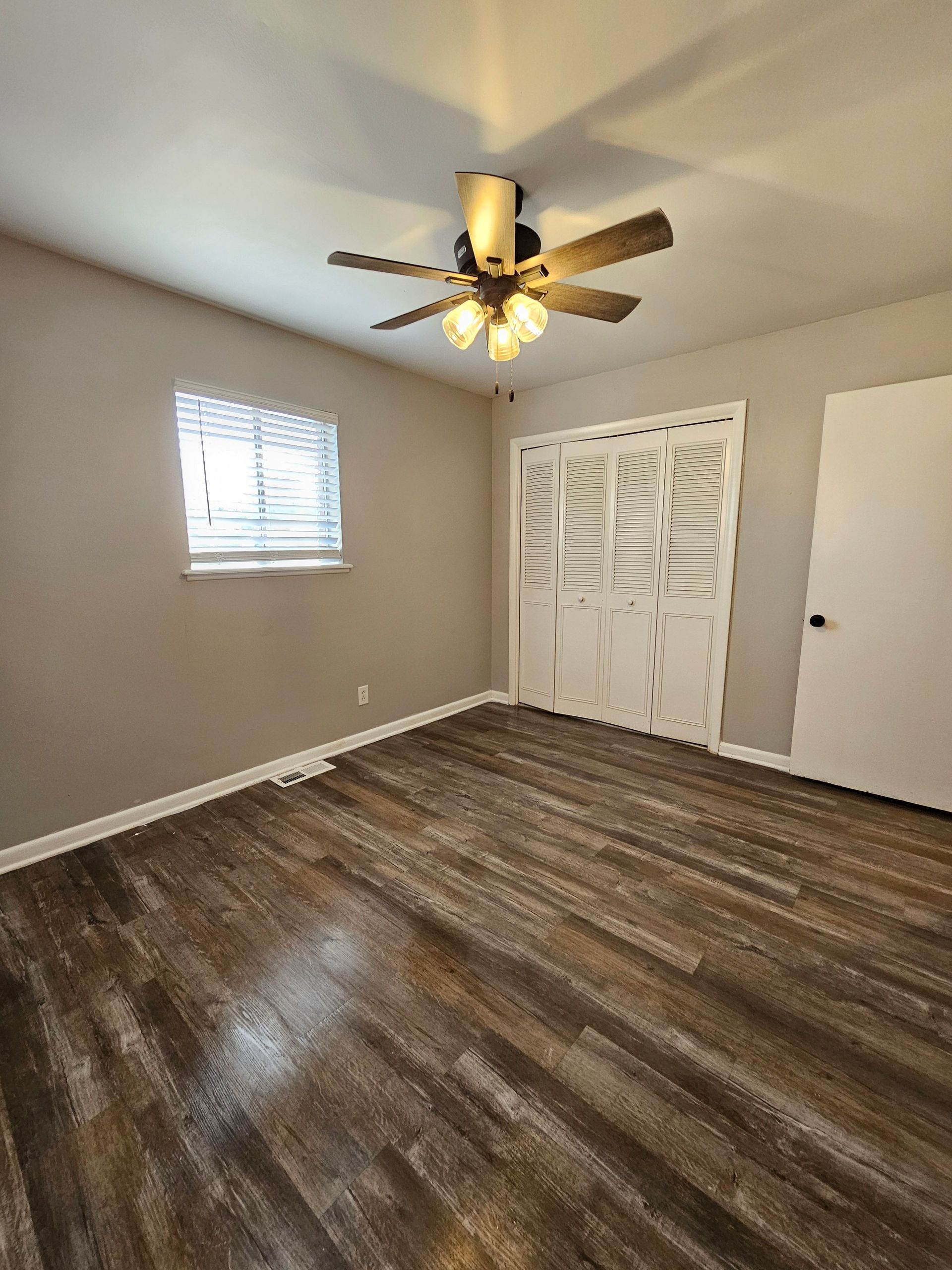 An empty bedroom with a ceiling fan and a window.