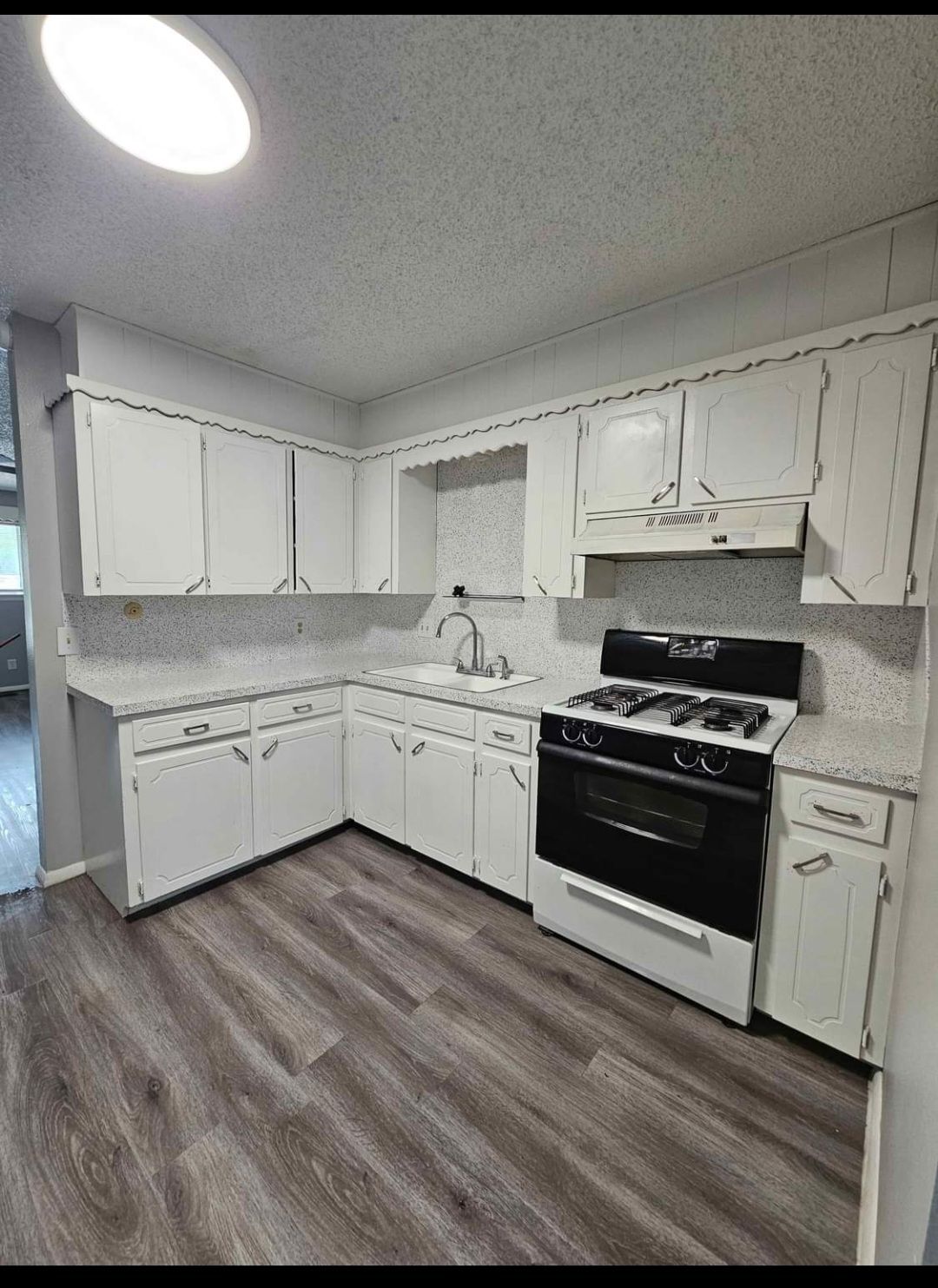A kitchen with white cabinets , a stove , and a sink.