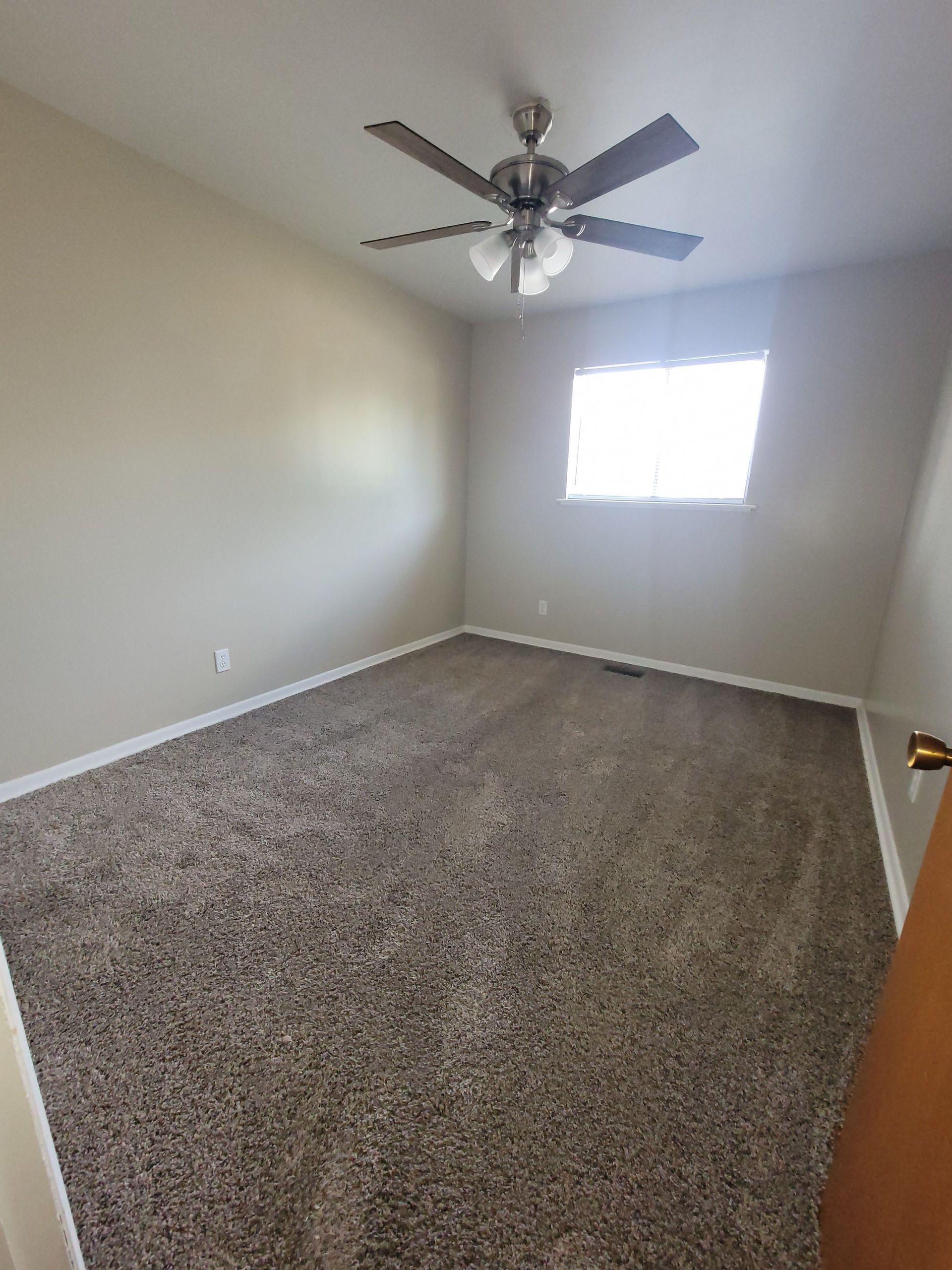 An empty bedroom with a ceiling fan and a window.