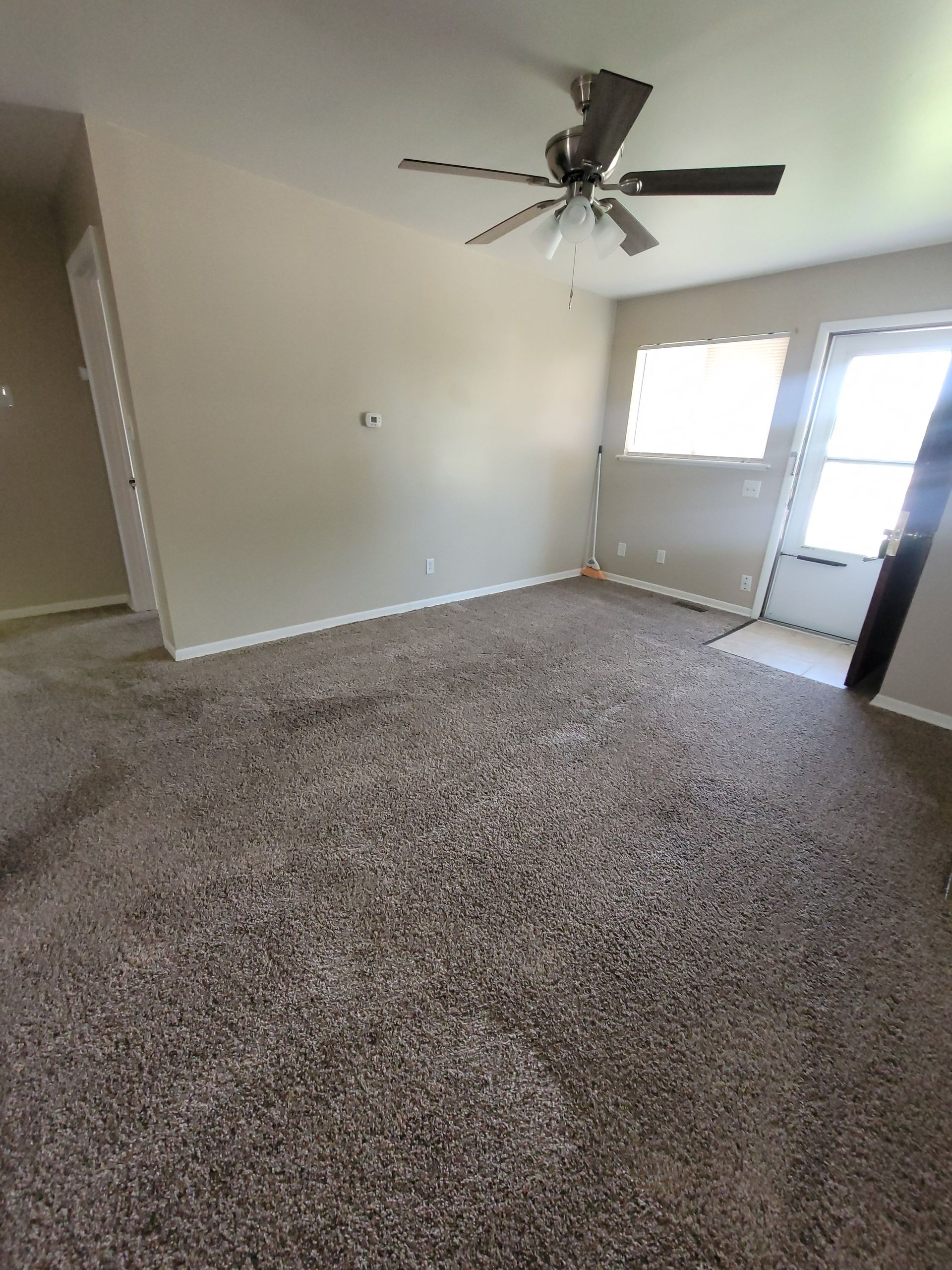 An empty living room with a ceiling fan and a door.