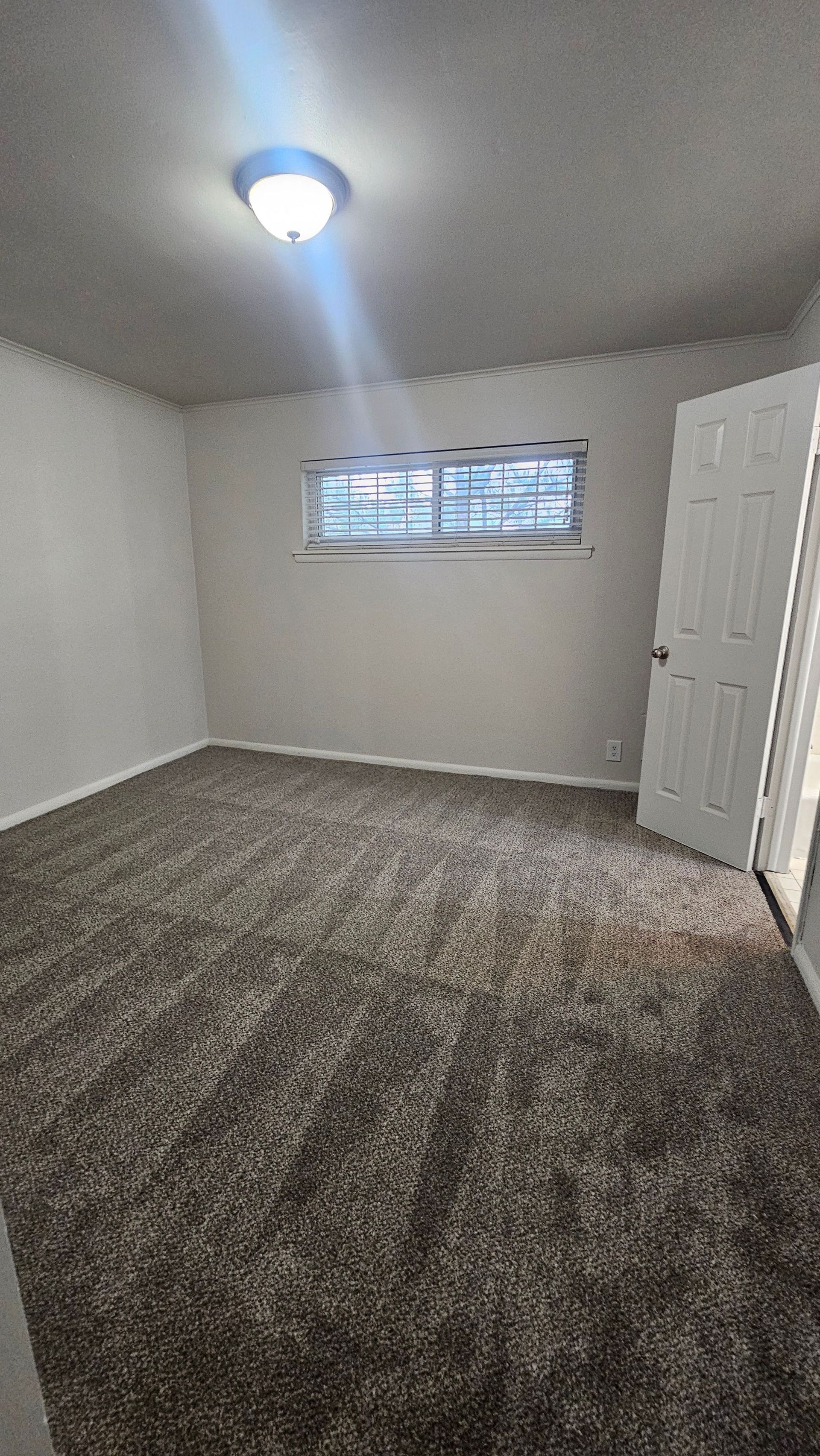 An empty bedroom with a window and a ceiling light.