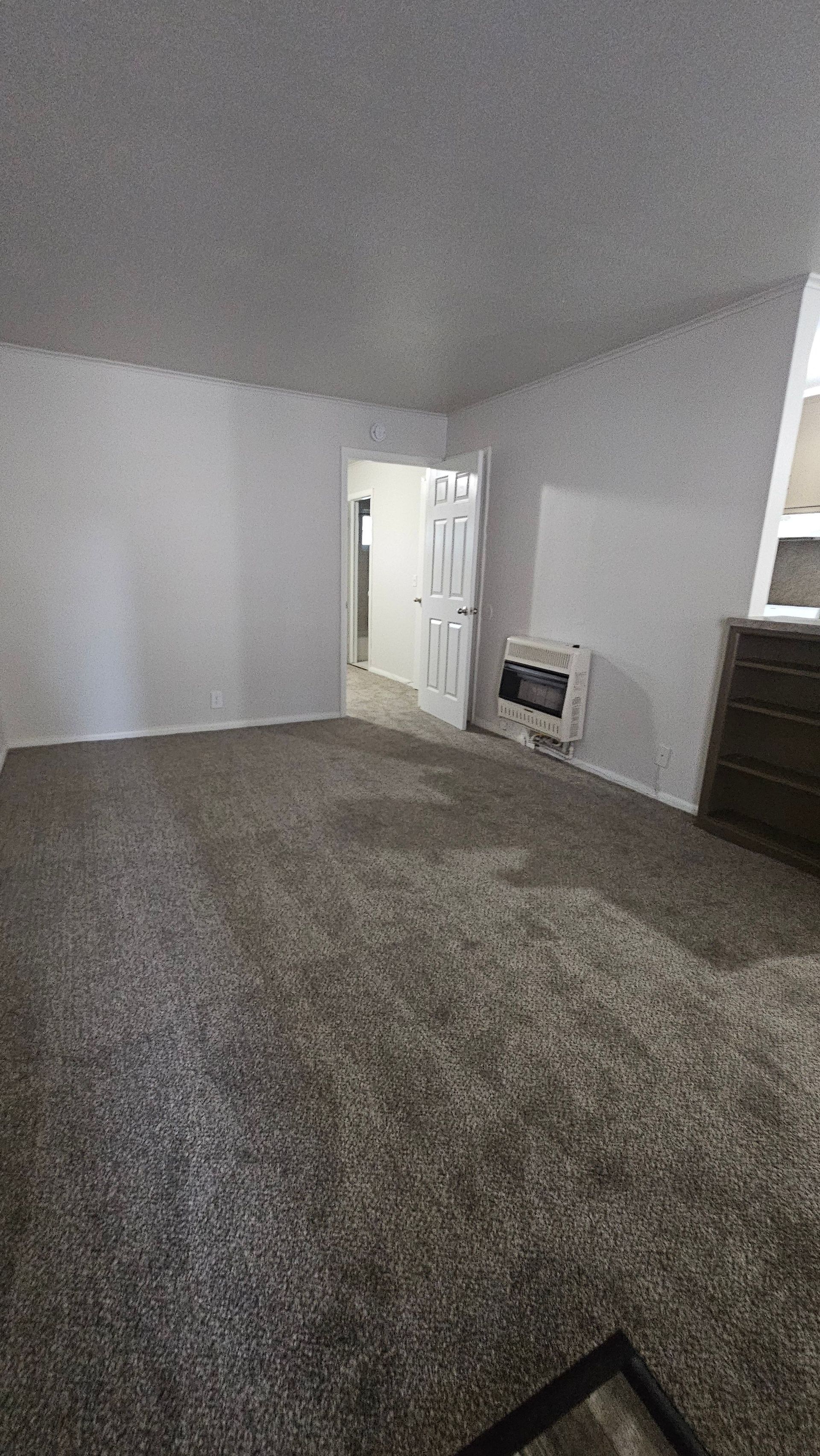 An empty living room with a carpeted floor and a fireplace.