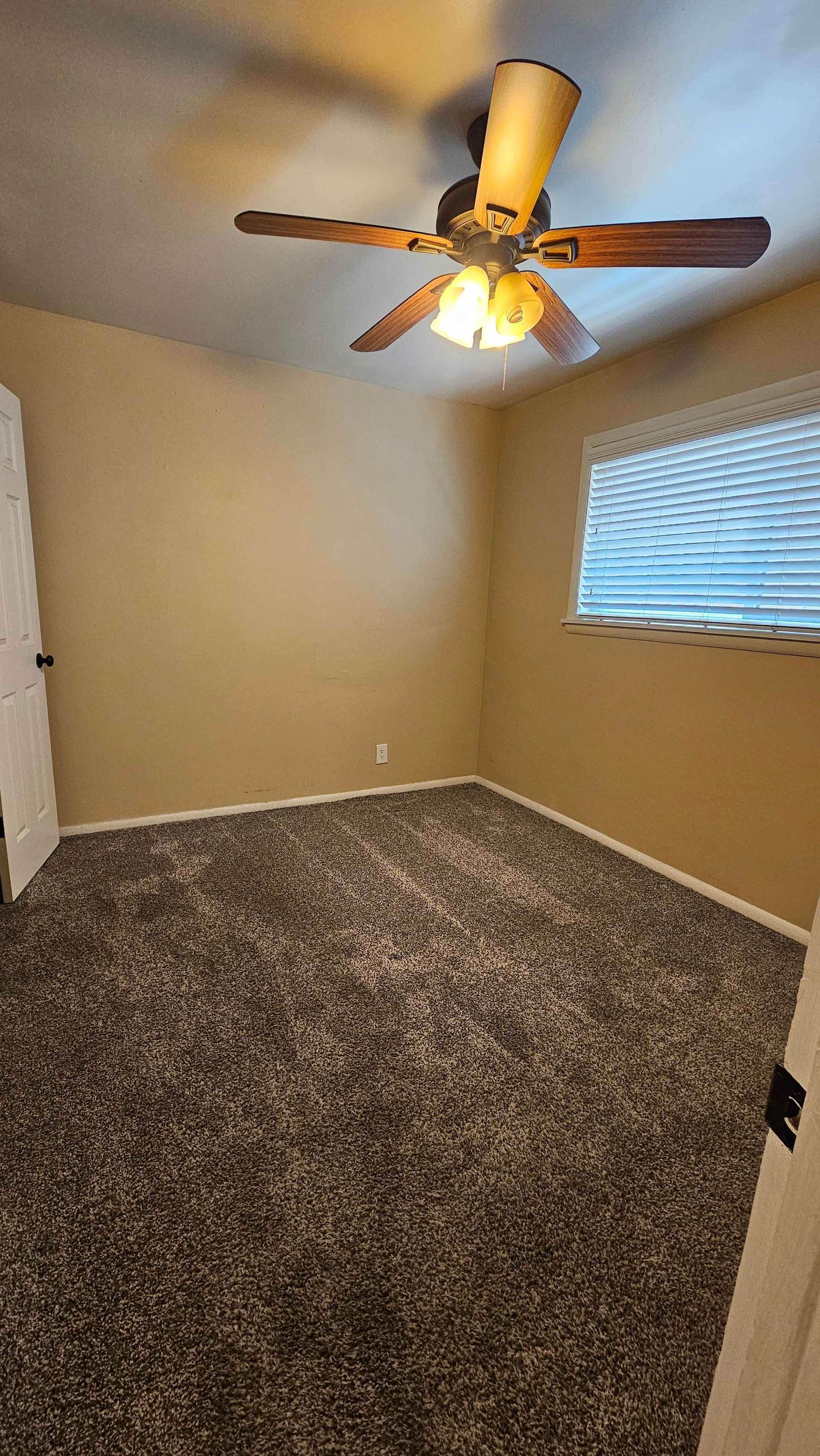 An empty bedroom with a ceiling fan and a window.