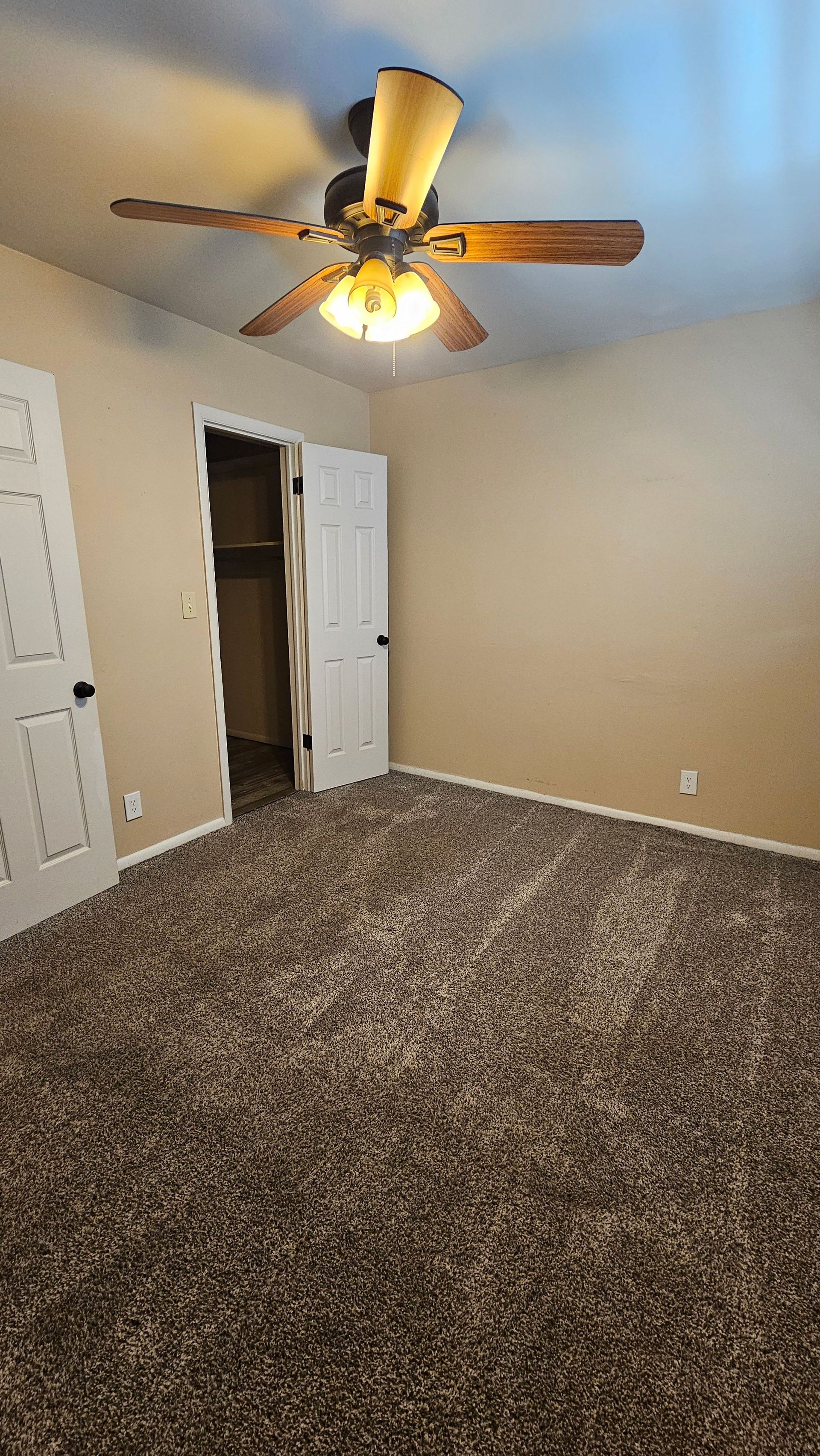 An empty bedroom with a ceiling fan and a closet.
