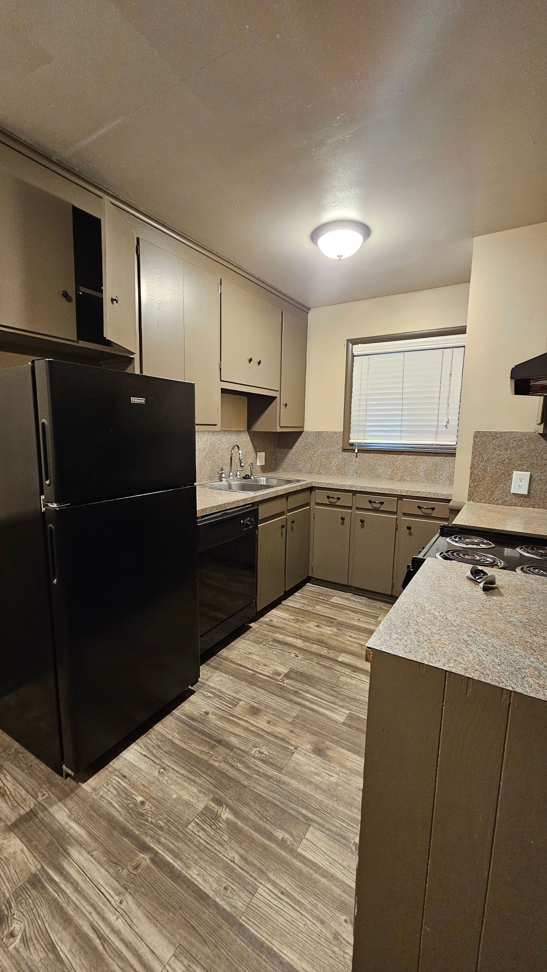 A kitchen with a black refrigerator , stove , dishwasher , sink and window.