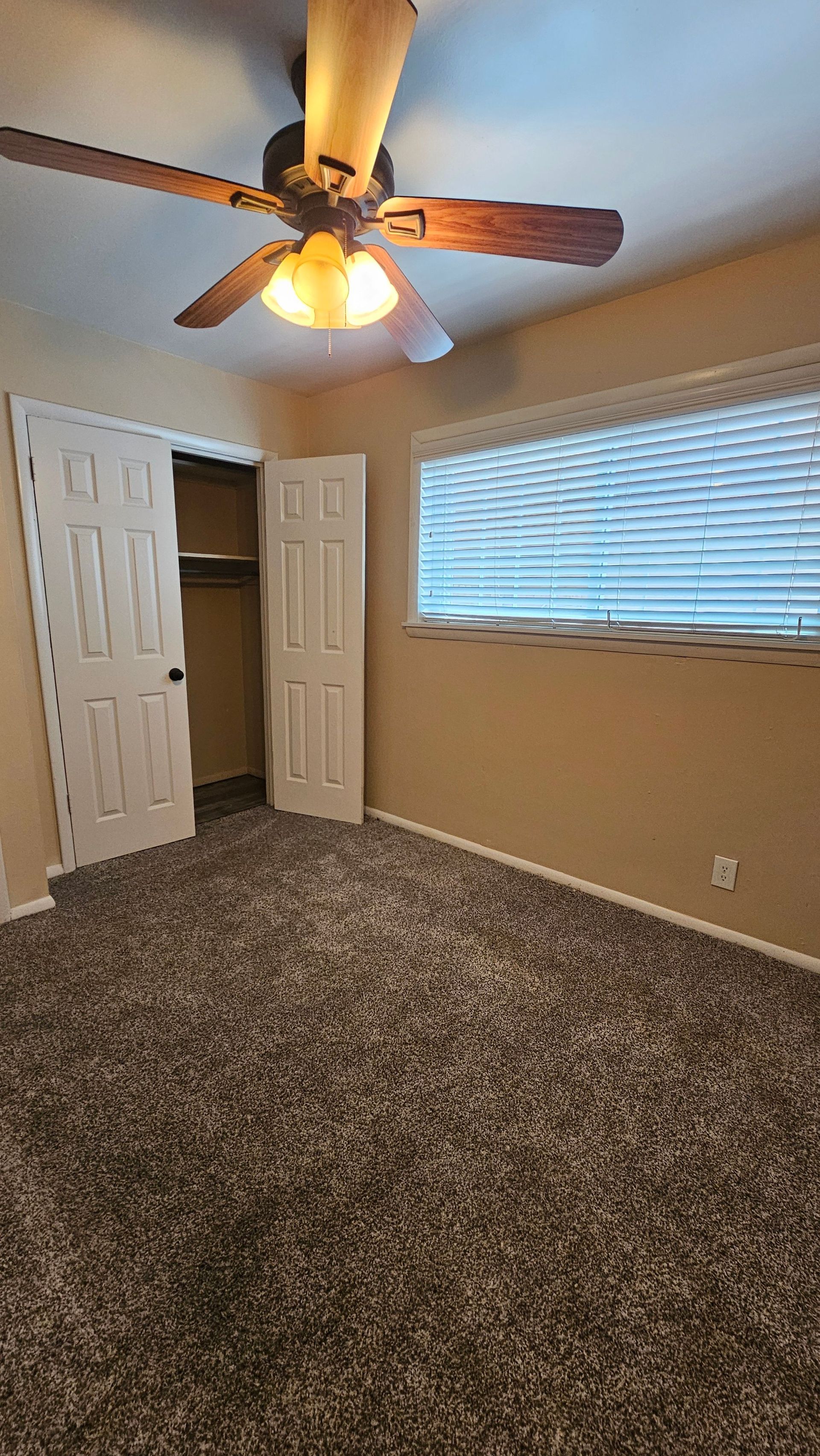 An empty bedroom with a ceiling fan and a window.