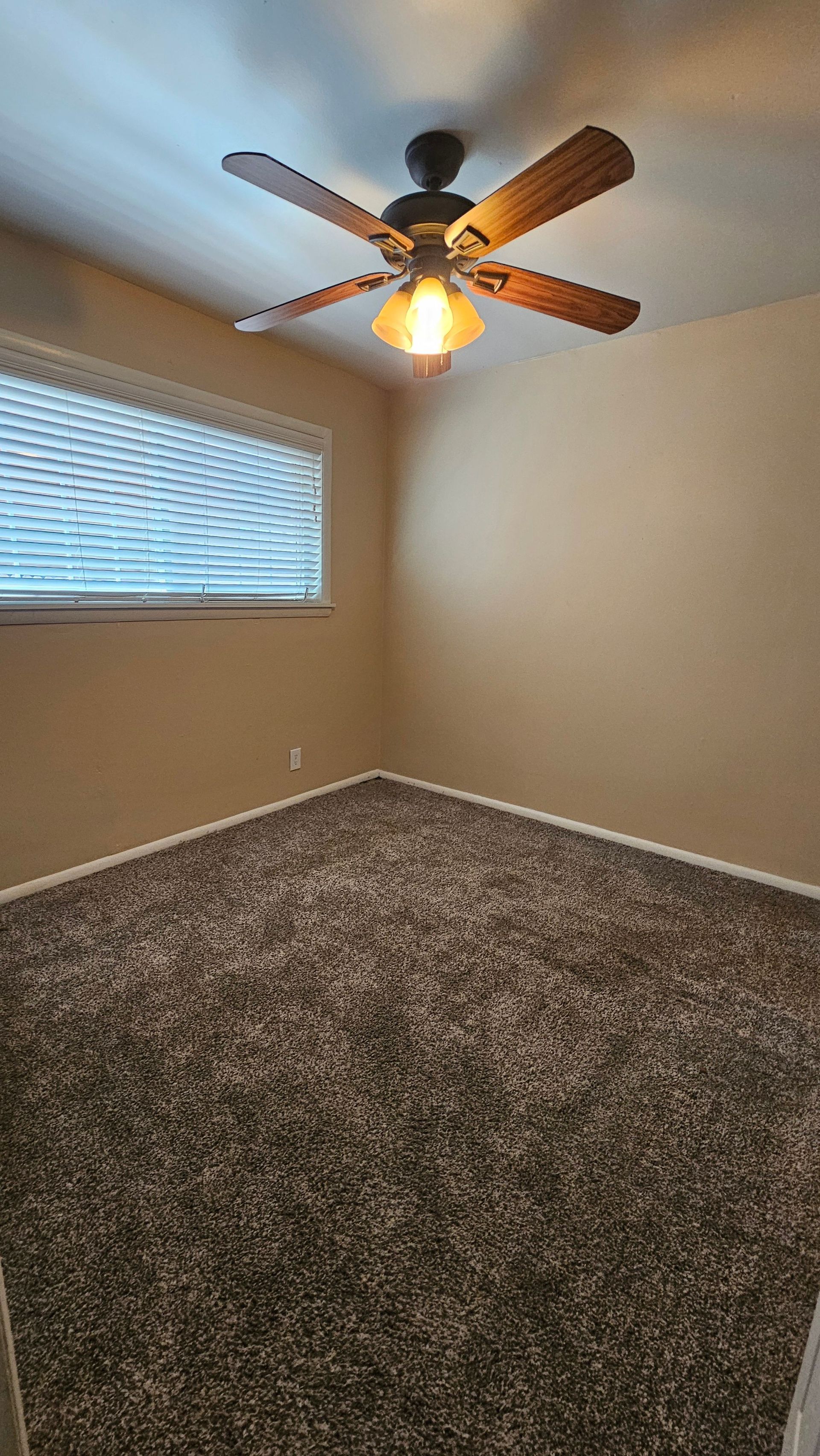 An empty bedroom with a ceiling fan and a window.