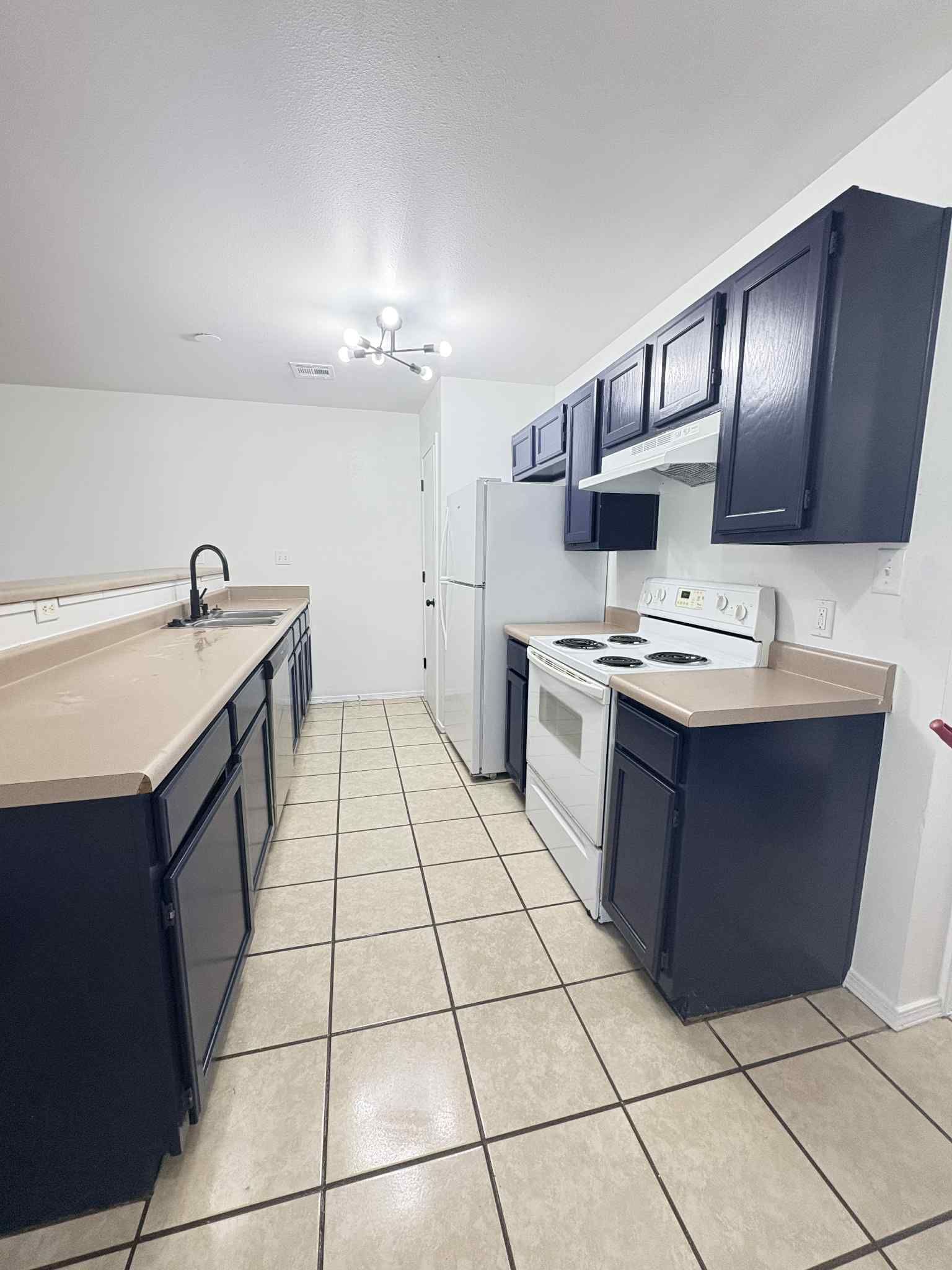 A kitchen with black cabinets , a stove , a refrigerator , and a sink.