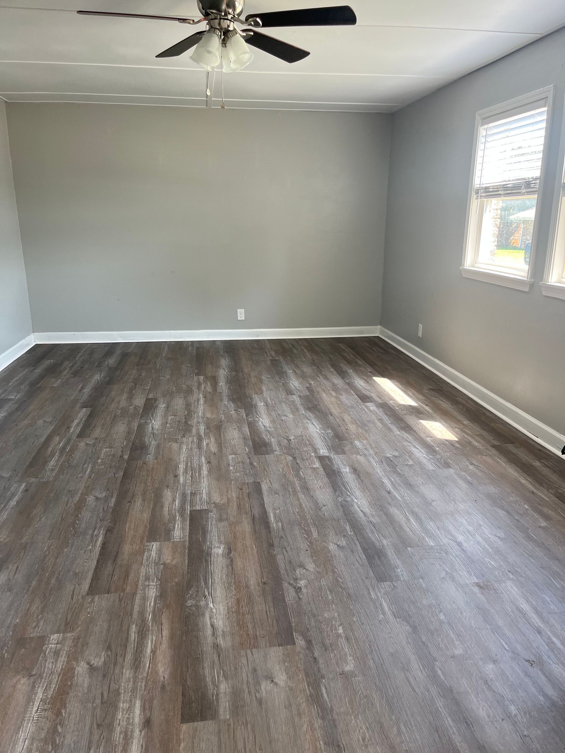 An empty living room with hardwood floors and a ceiling fan.